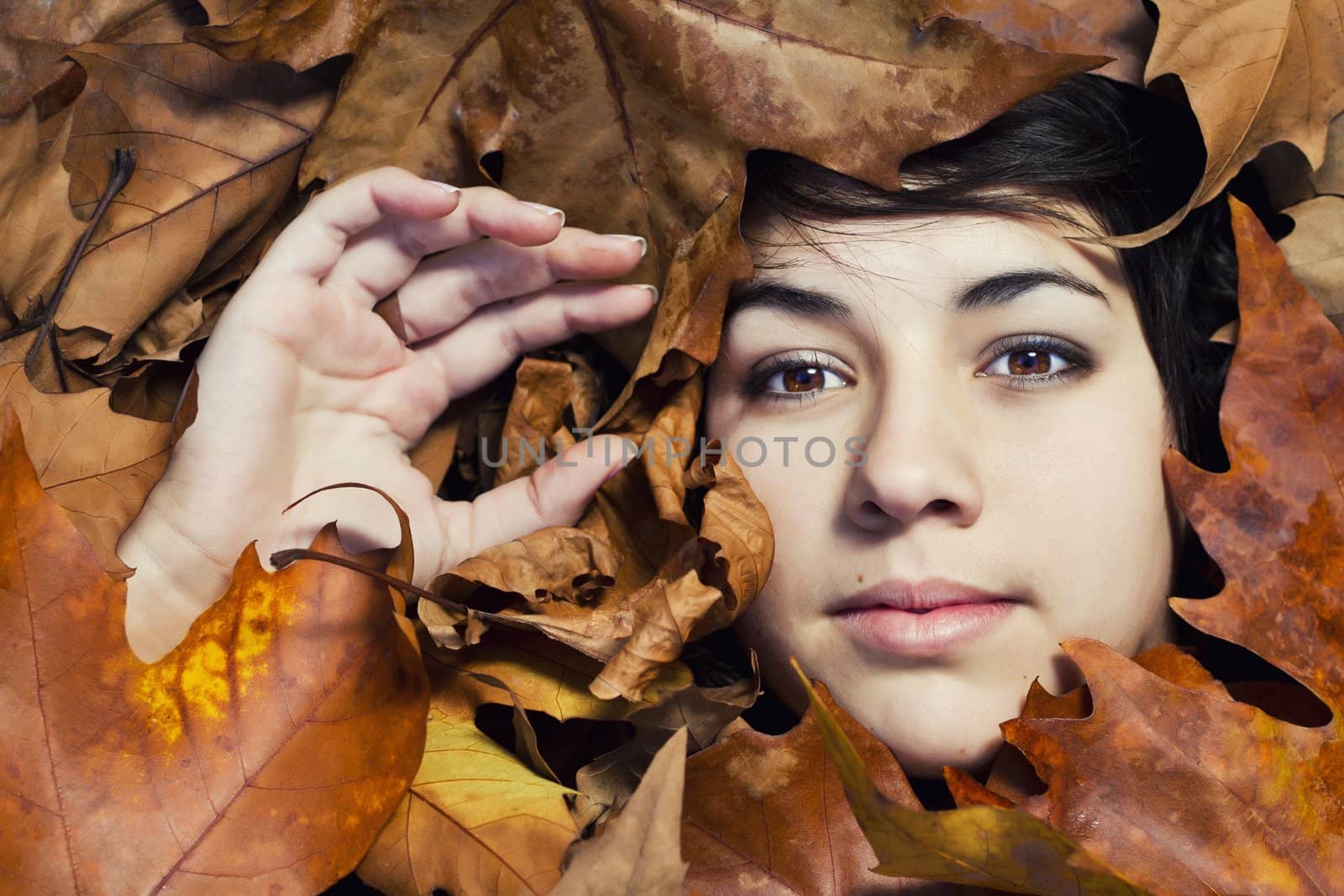 Close view of the face of a beautiful girl surrounded by autumn leaves.