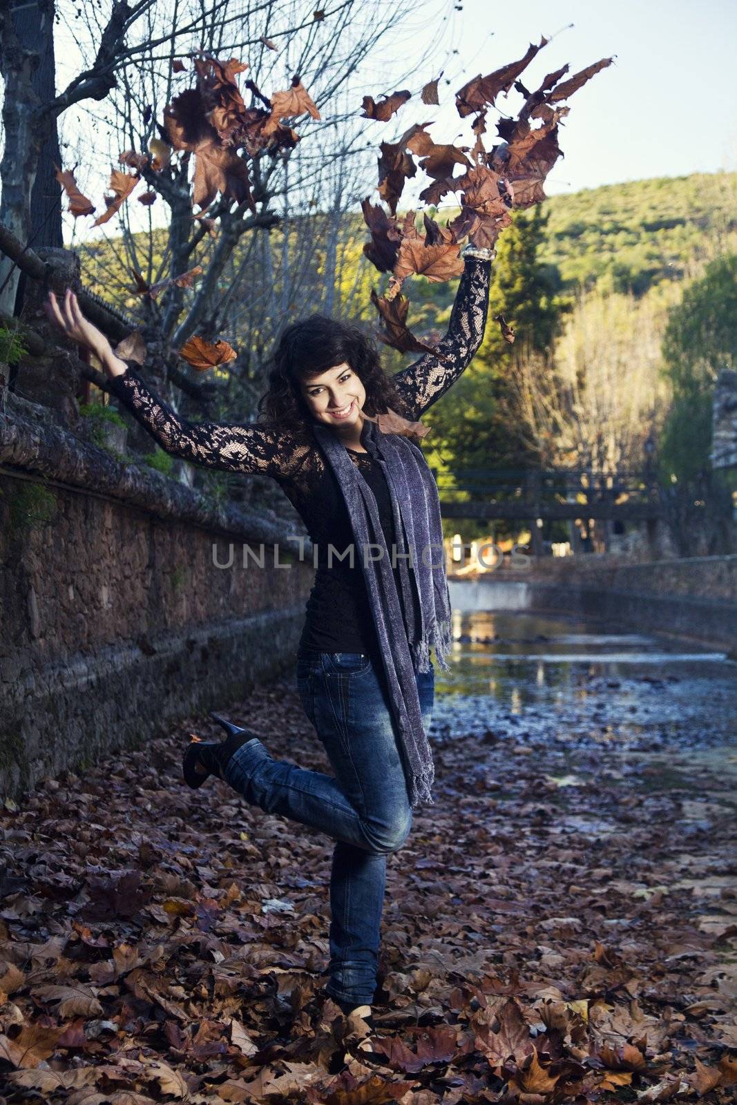 Beautiful girl throws in the air a bunch of autumn leaves.