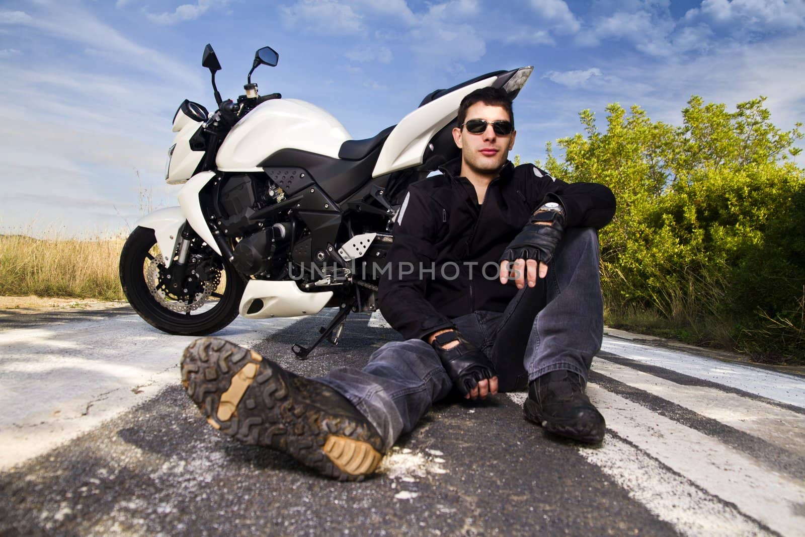View of a man with a motorcycle on a asphalt road.