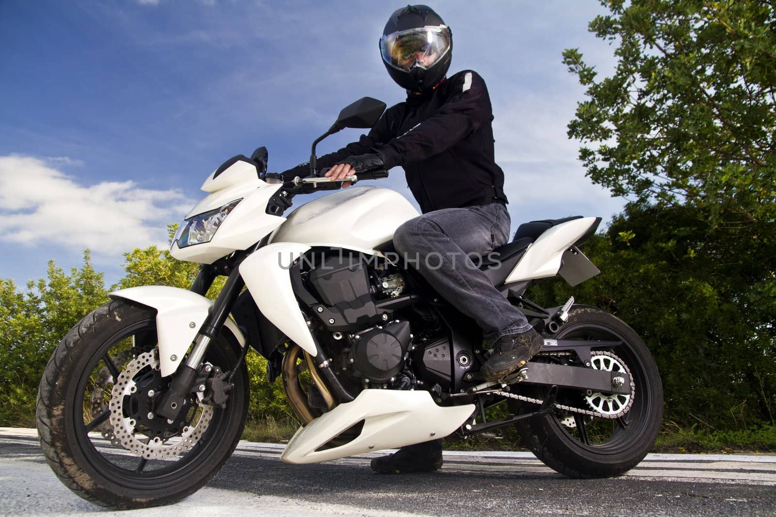 View of a man with a motorcycle on a asphalt road.