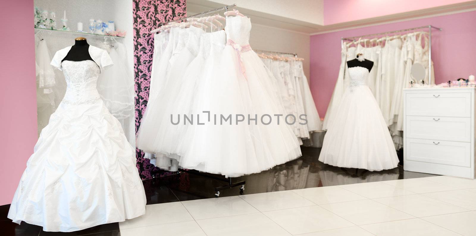 Wedding store panorama. Shallow depth of field. White bridal dresses. Artificial flowers and different stuff on glass shelfs