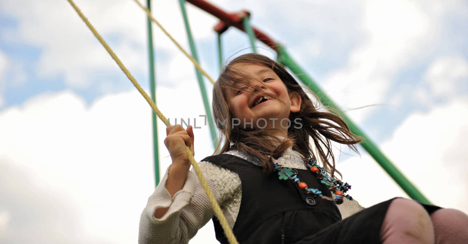 happy young girl on her swing on a cloudy sky