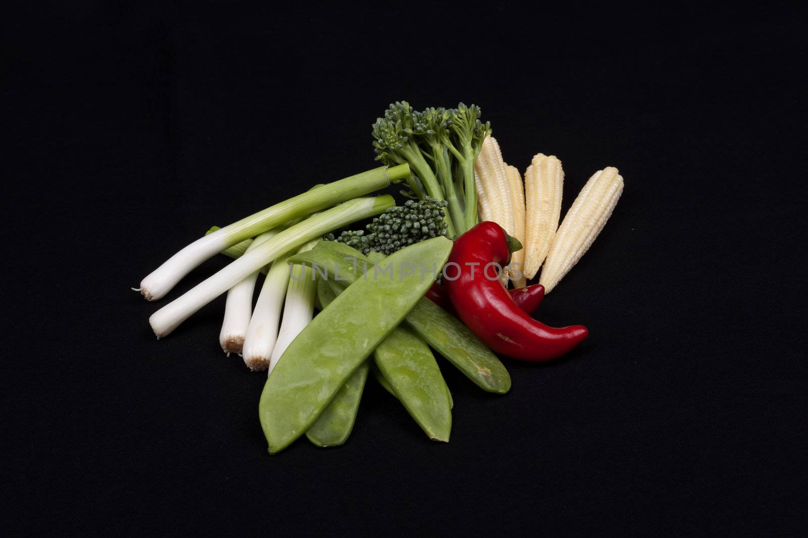 chilli, broccoli, baby leek, baby corn and mange tout on a black background