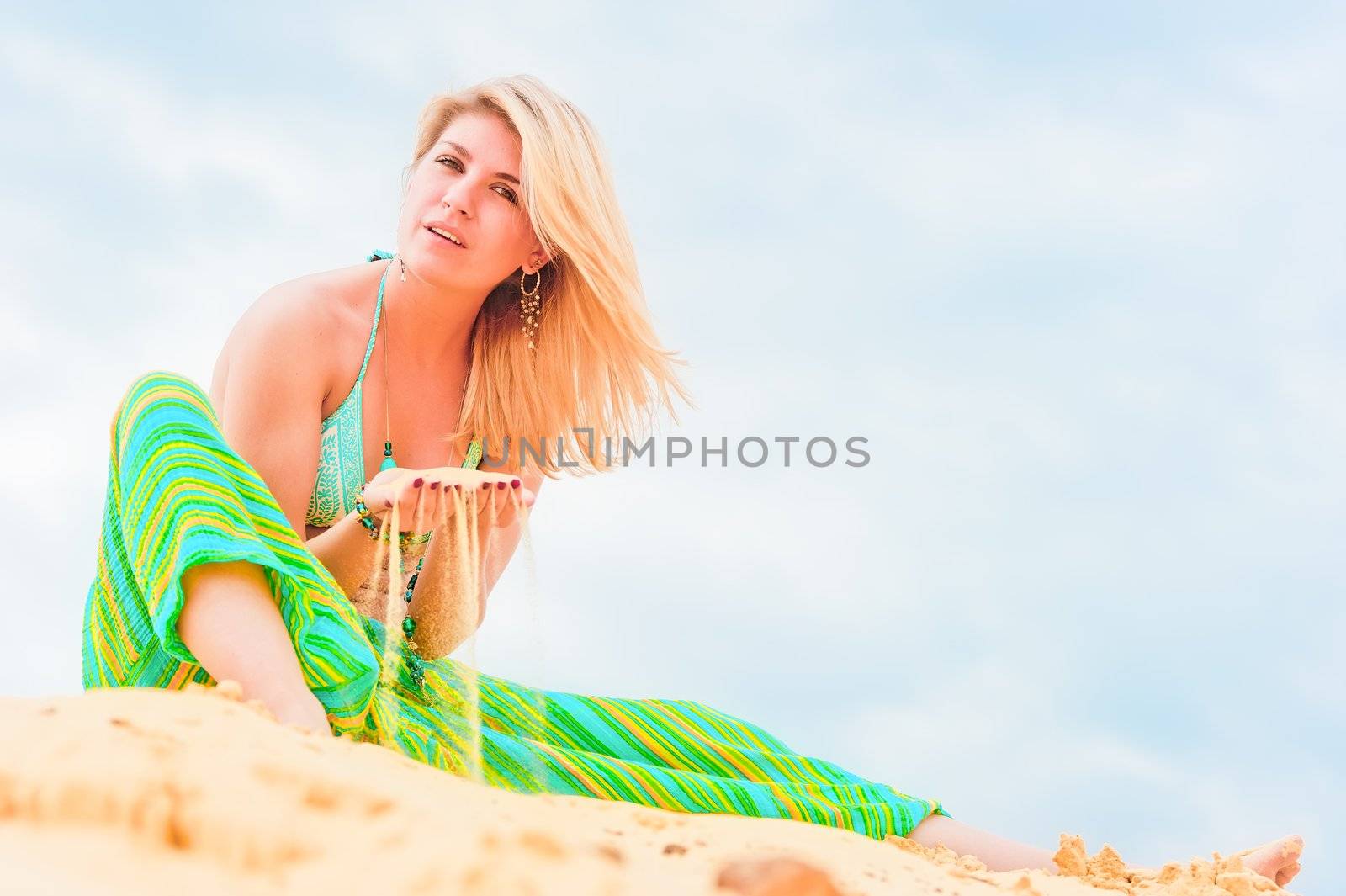 Young blonde girl sitting on the sand in the sky.