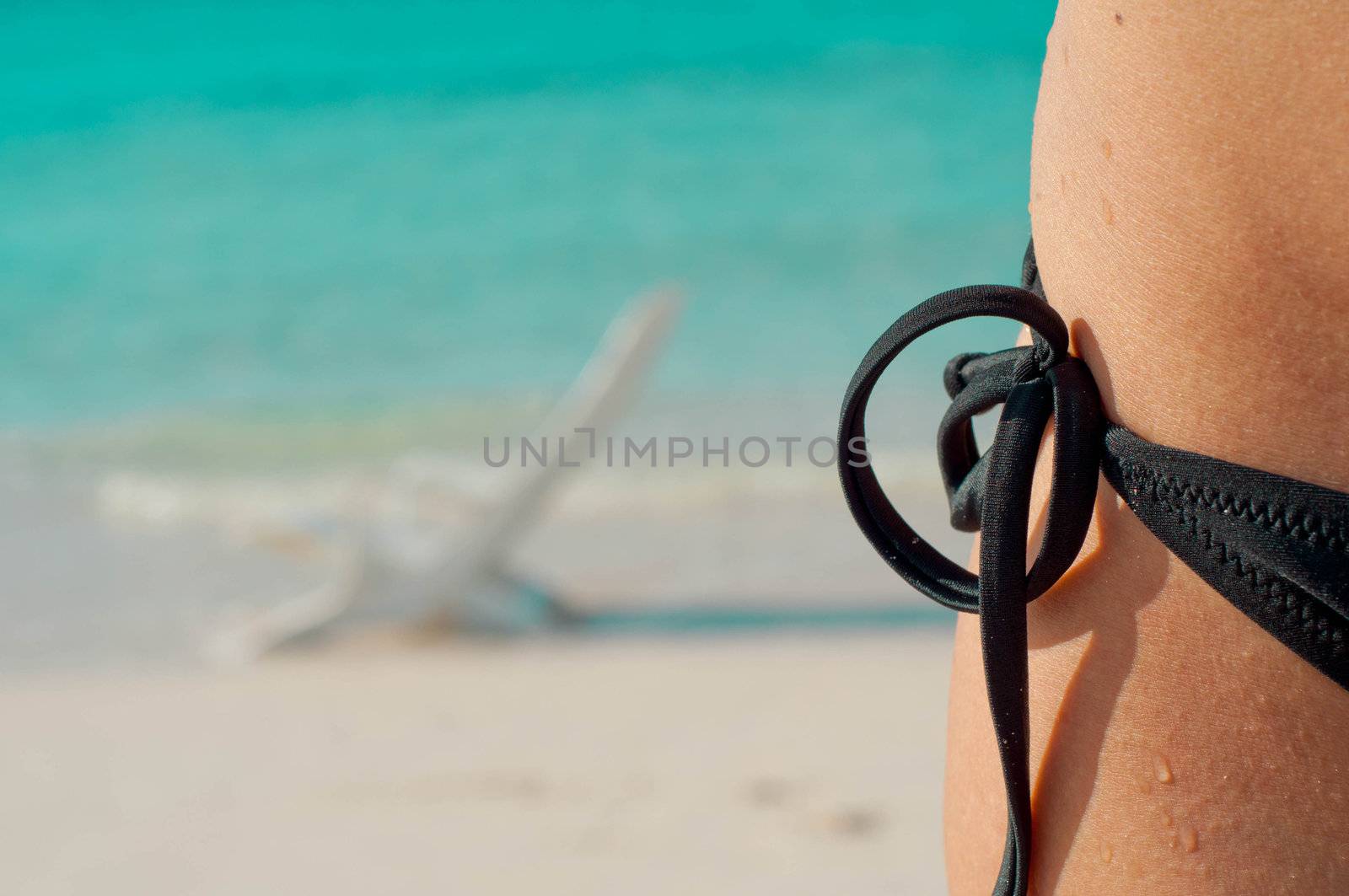 Image of a woman's hip with a bikini against a beach background.