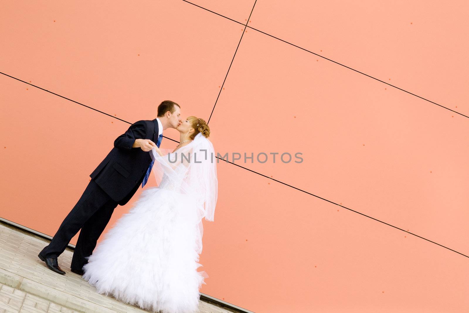 bride and groom by the red wall