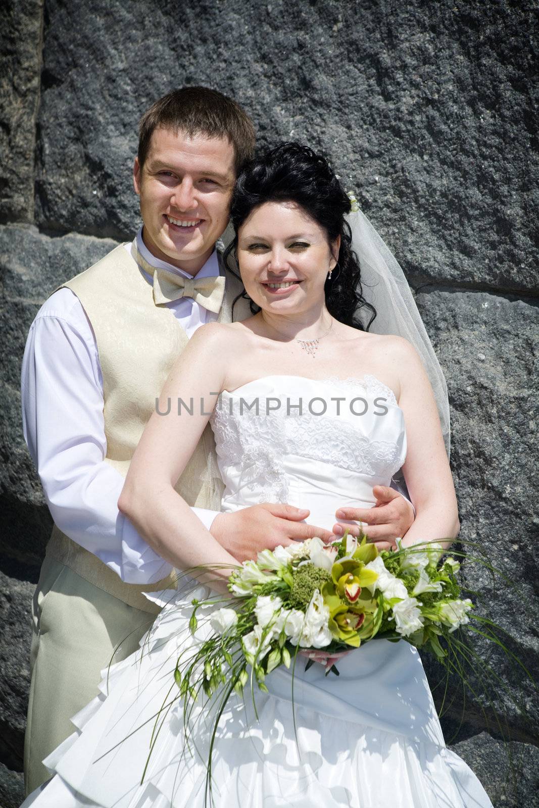 happy newl married couple near the stone wall