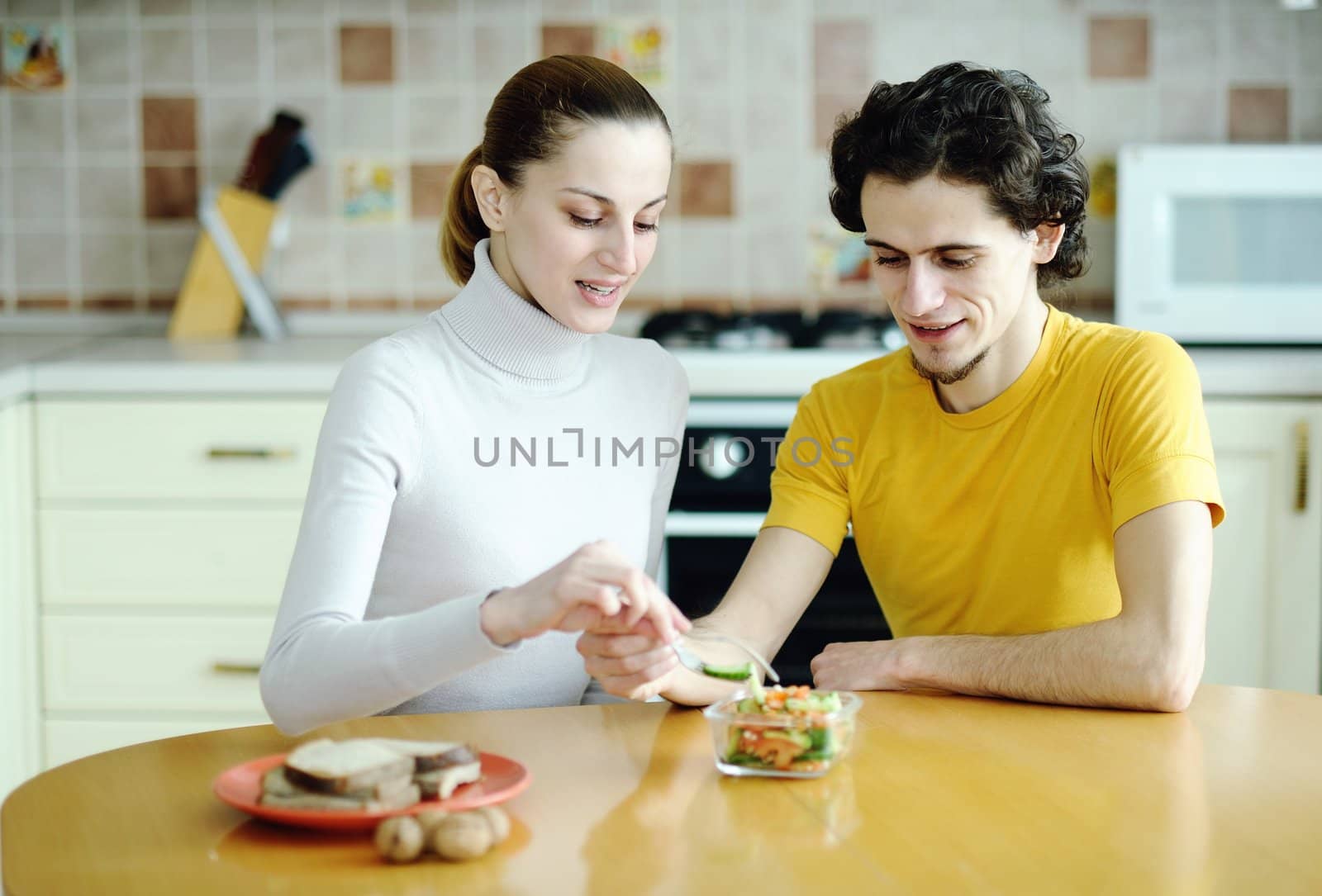 Funny scene of young happy couple playfully eating at kitchen