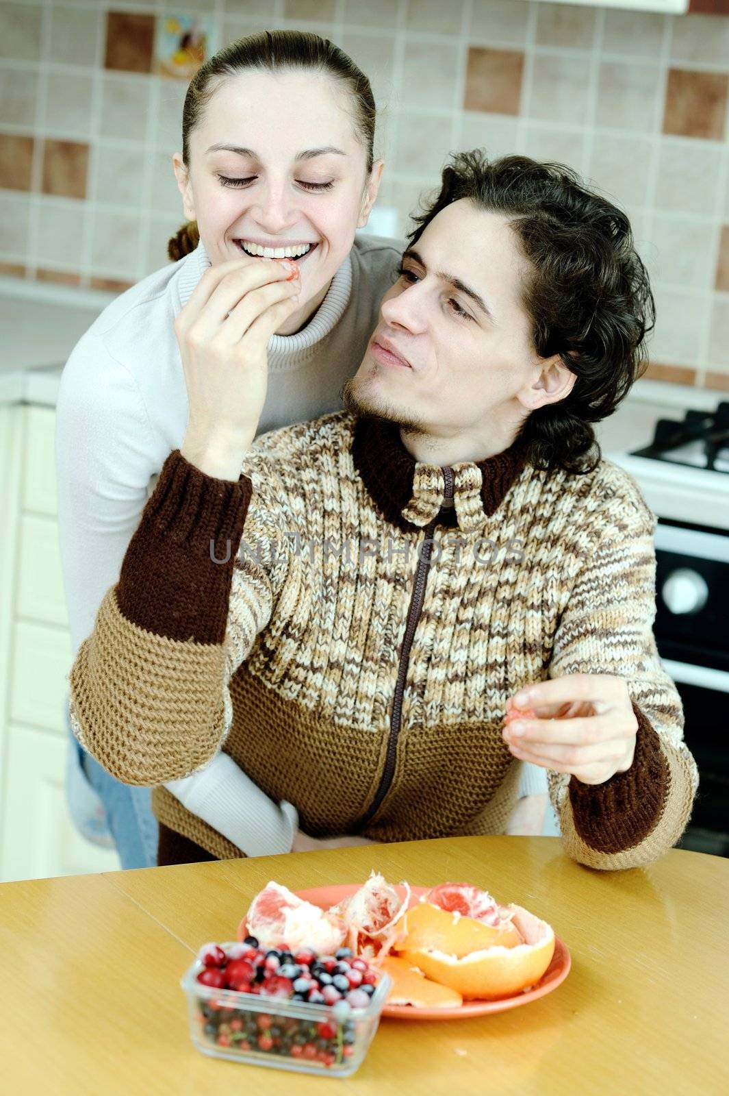 Funny scene of young happy couple playfully eating at kitchen