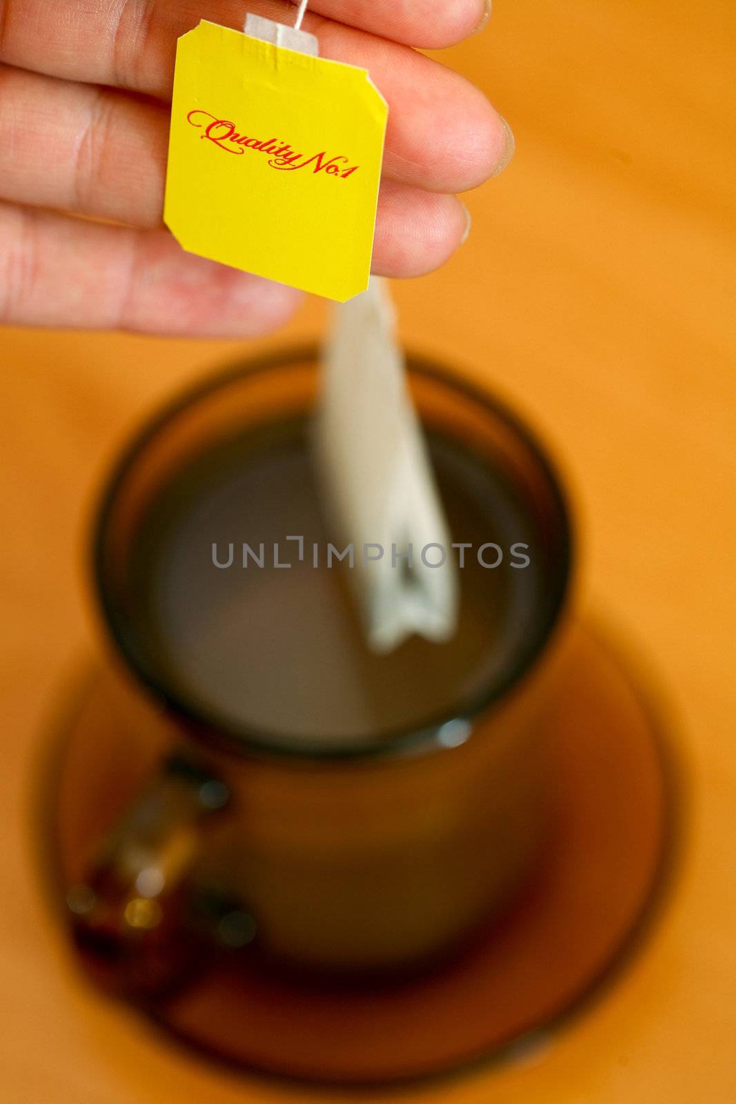 Womans hand holding tea bag on background of cup of tea