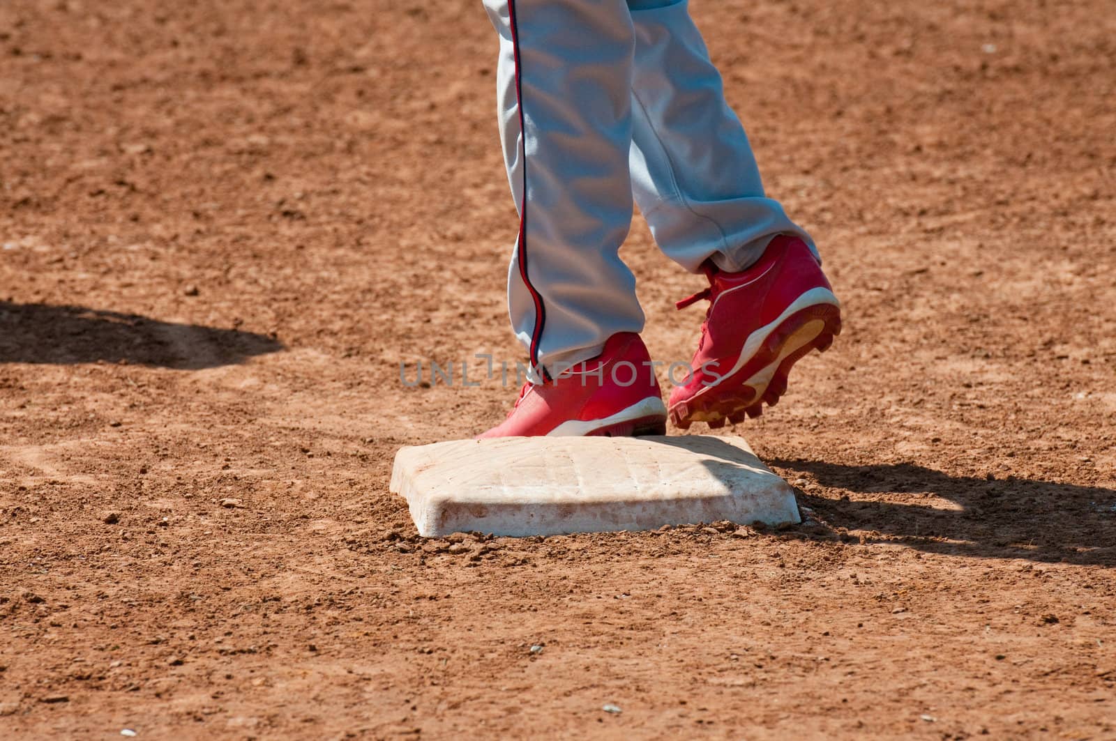 Lower body shot of a teen baseball player standing on base.