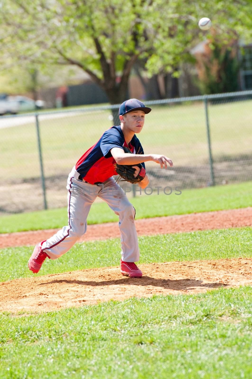 Teen baseball pitcher after the throw to the batter with the ball in the air.