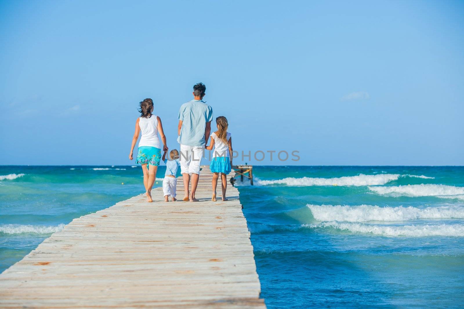 Family of four on wooden jetty by the ocean by maxoliki