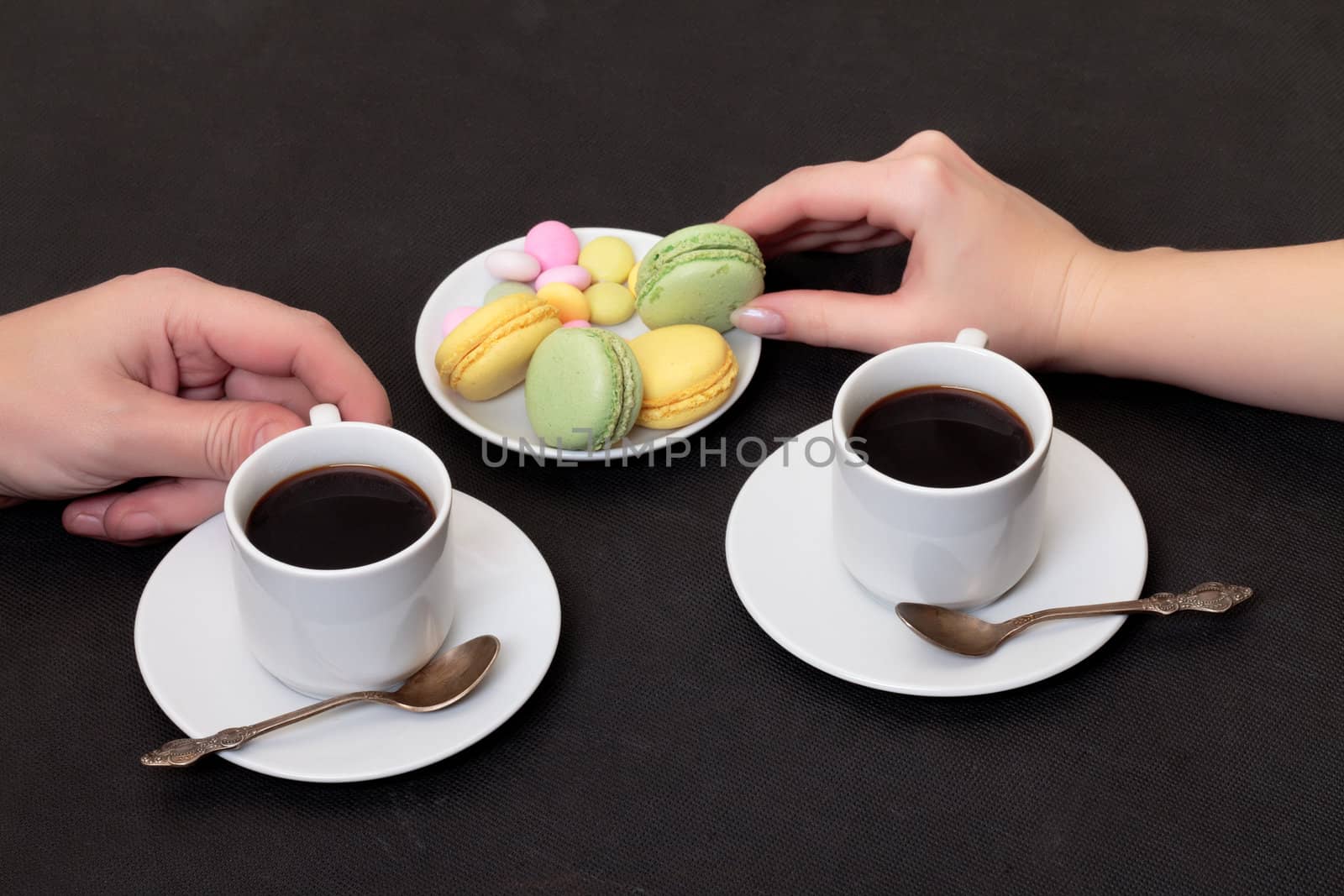 Couple drinking coffee with macaroon, on black
