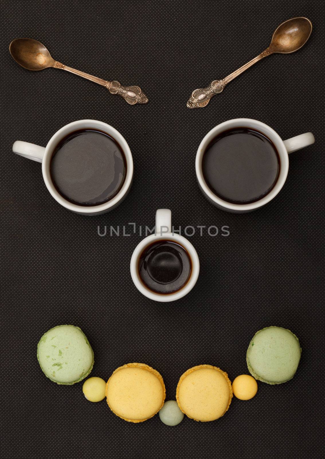 Tree cups coffee and macaroon arranged in happy face, on black