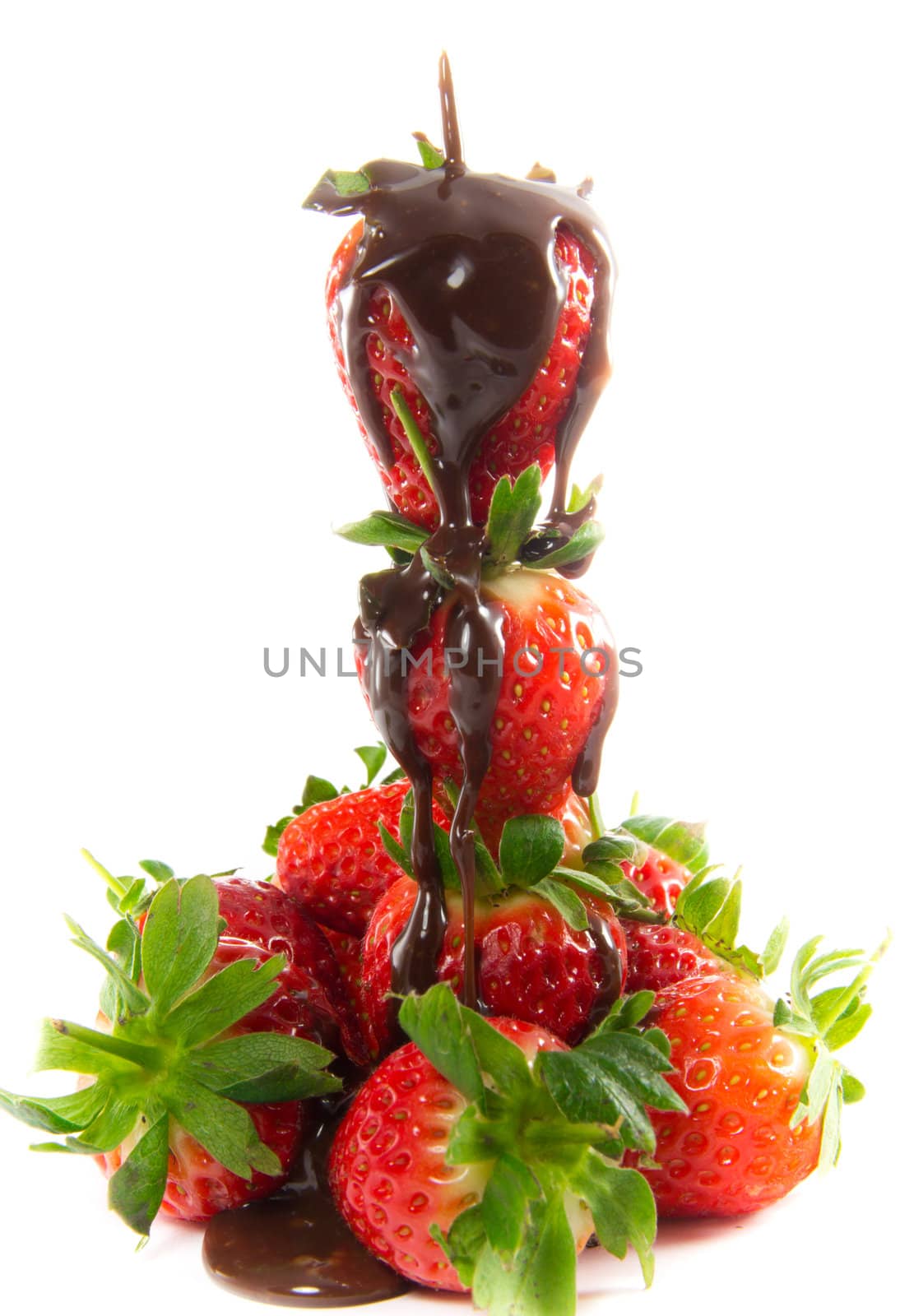 A picture of melted chocolate that is poured over a tower of strawberries