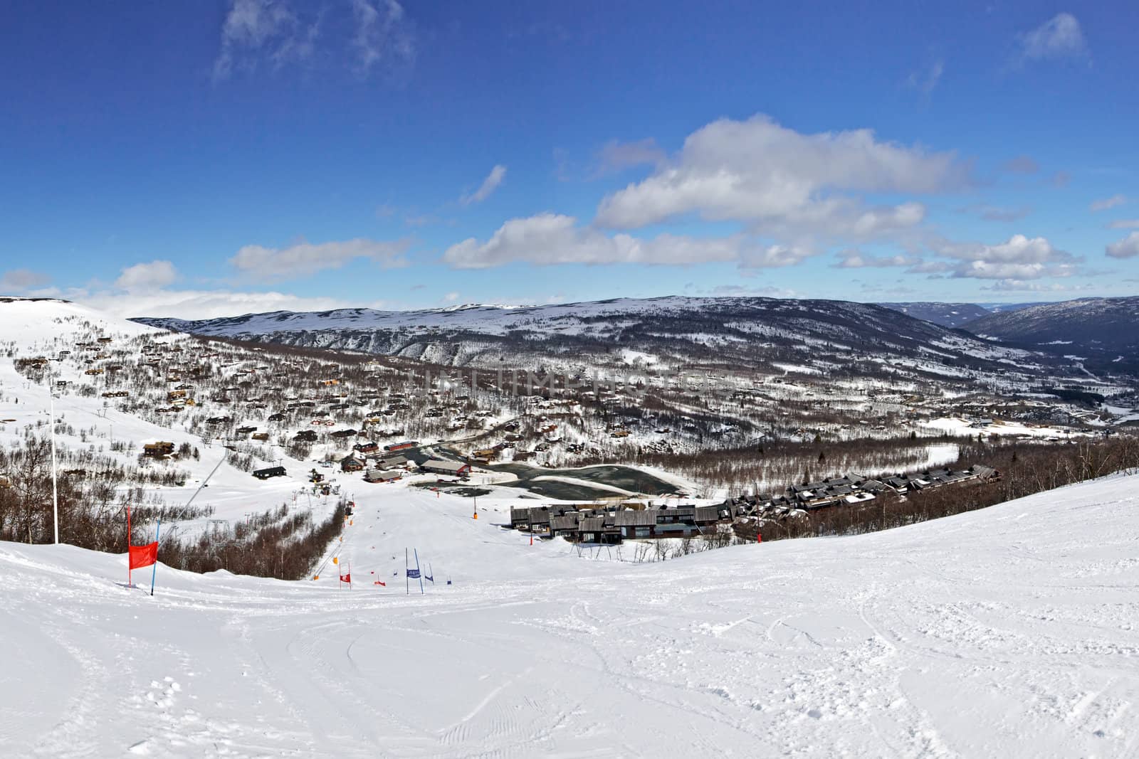 Panoramic view of ski route, village and sky  taken from slope in bright winter day