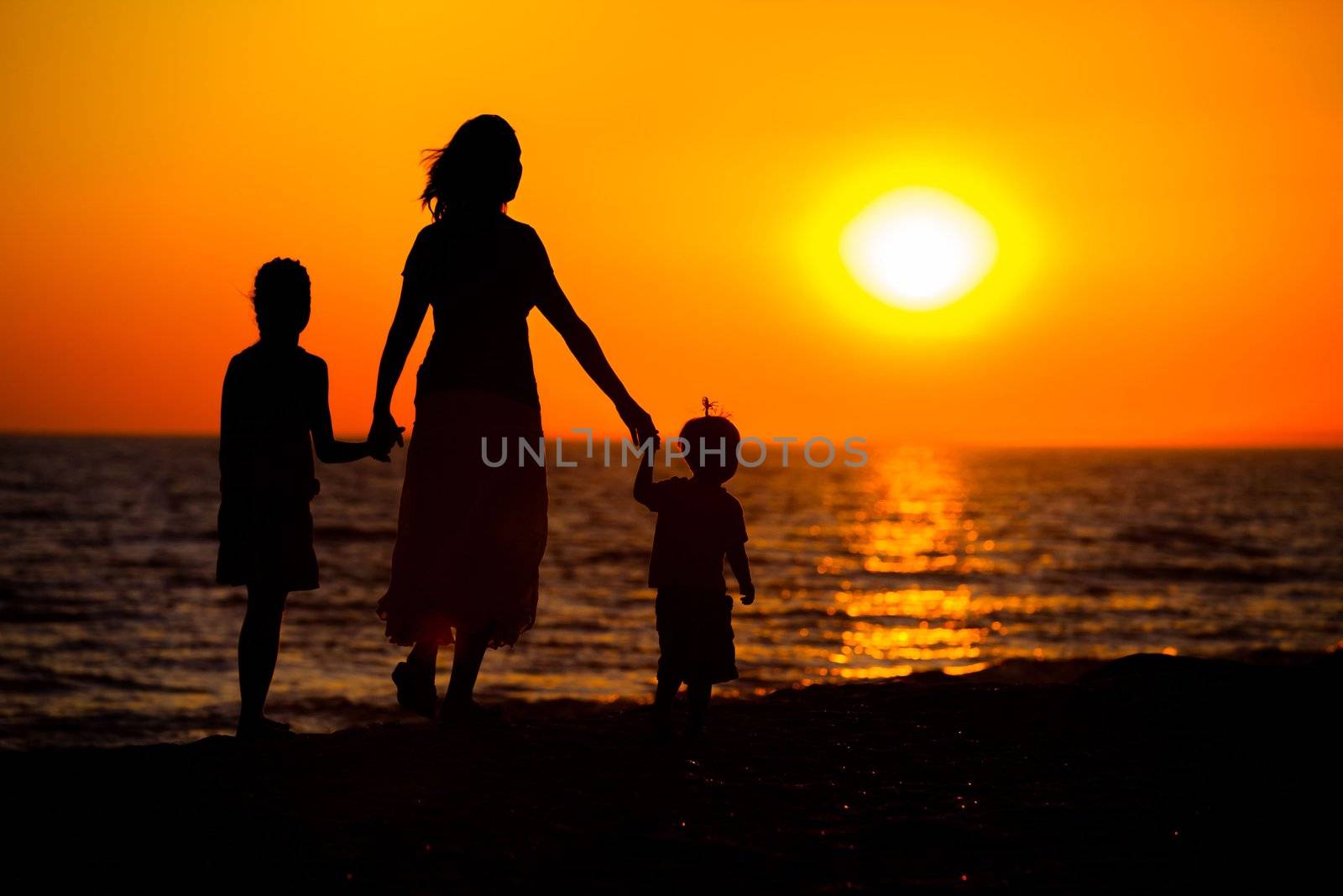 Mother and her kids silhouettes on beach at sunset