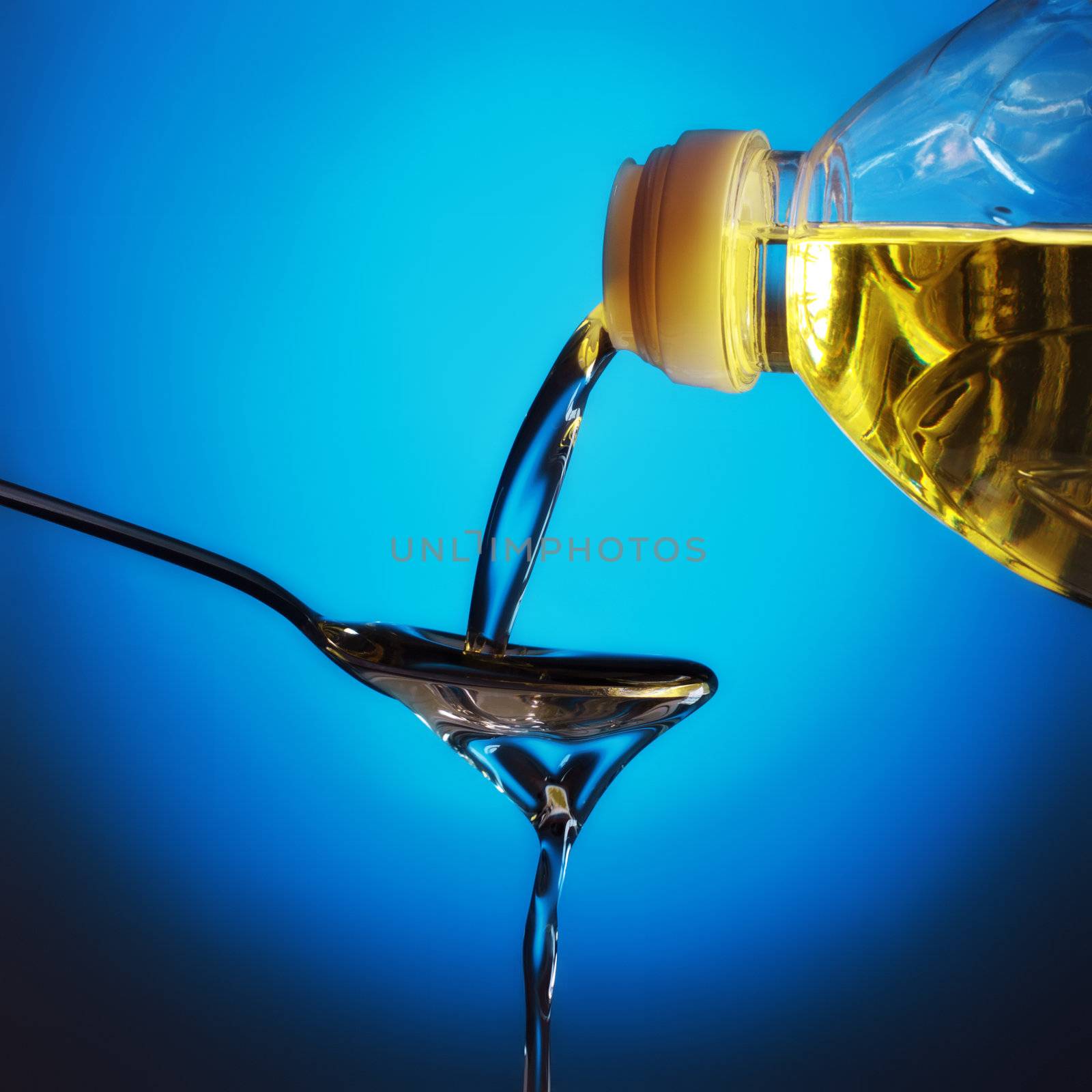 pouring olive oil on spoon, blue background