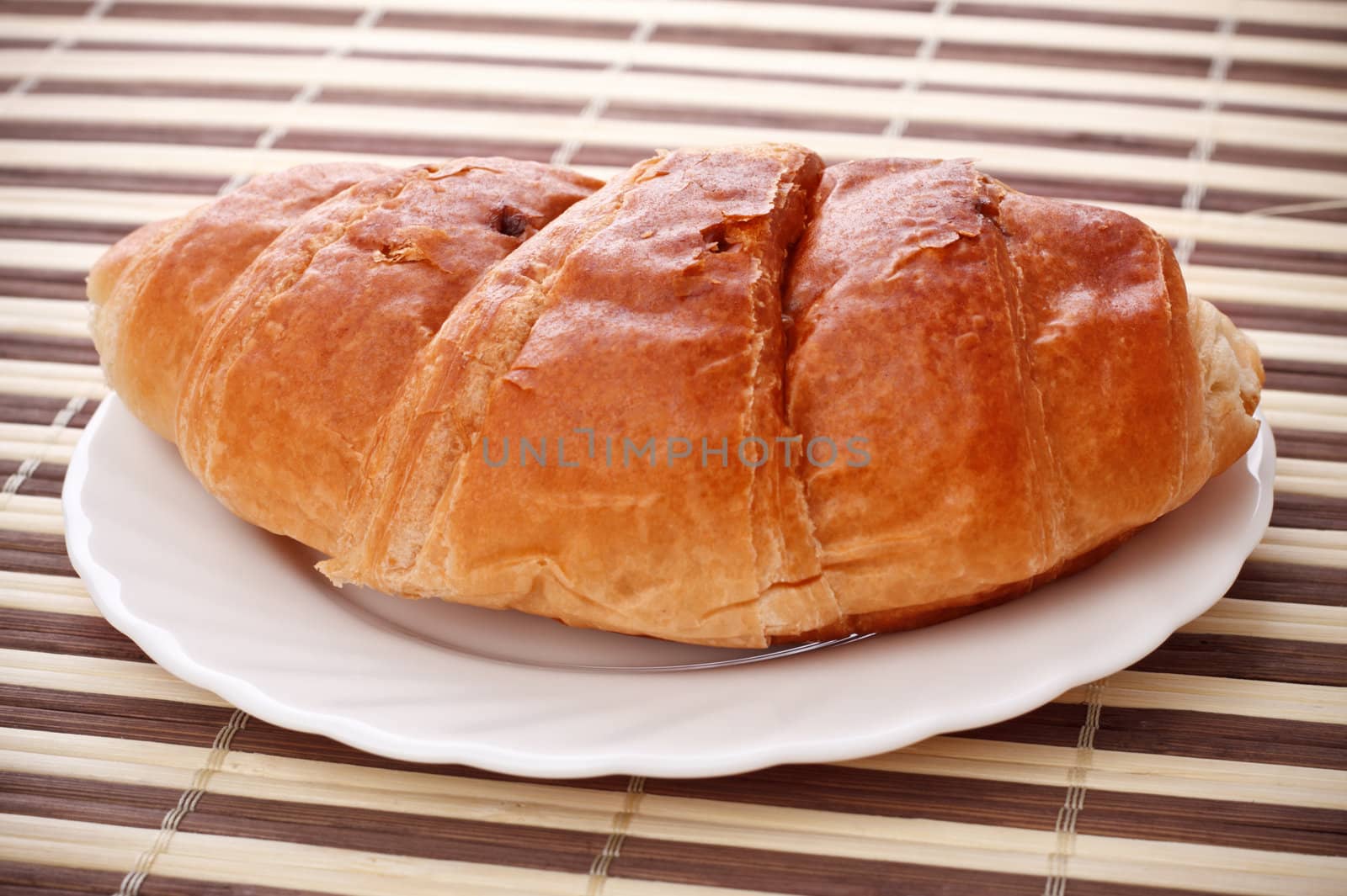 single fresh croissant laying on white dish