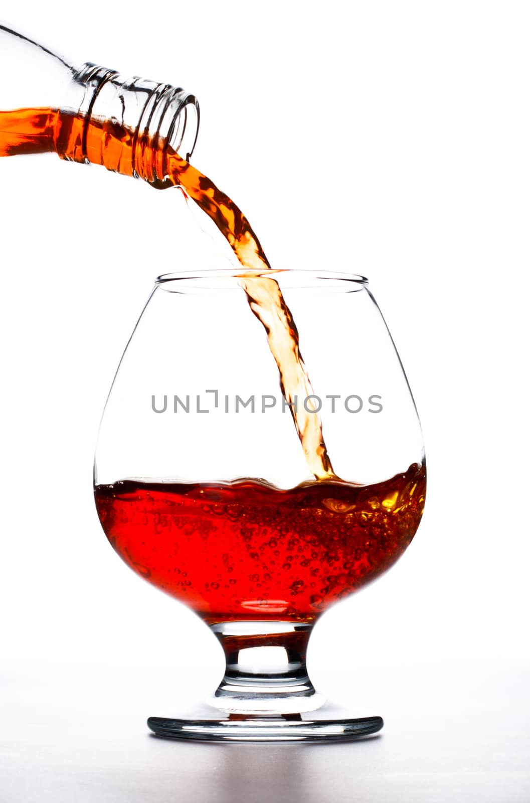 cognac pour into the glass over white background