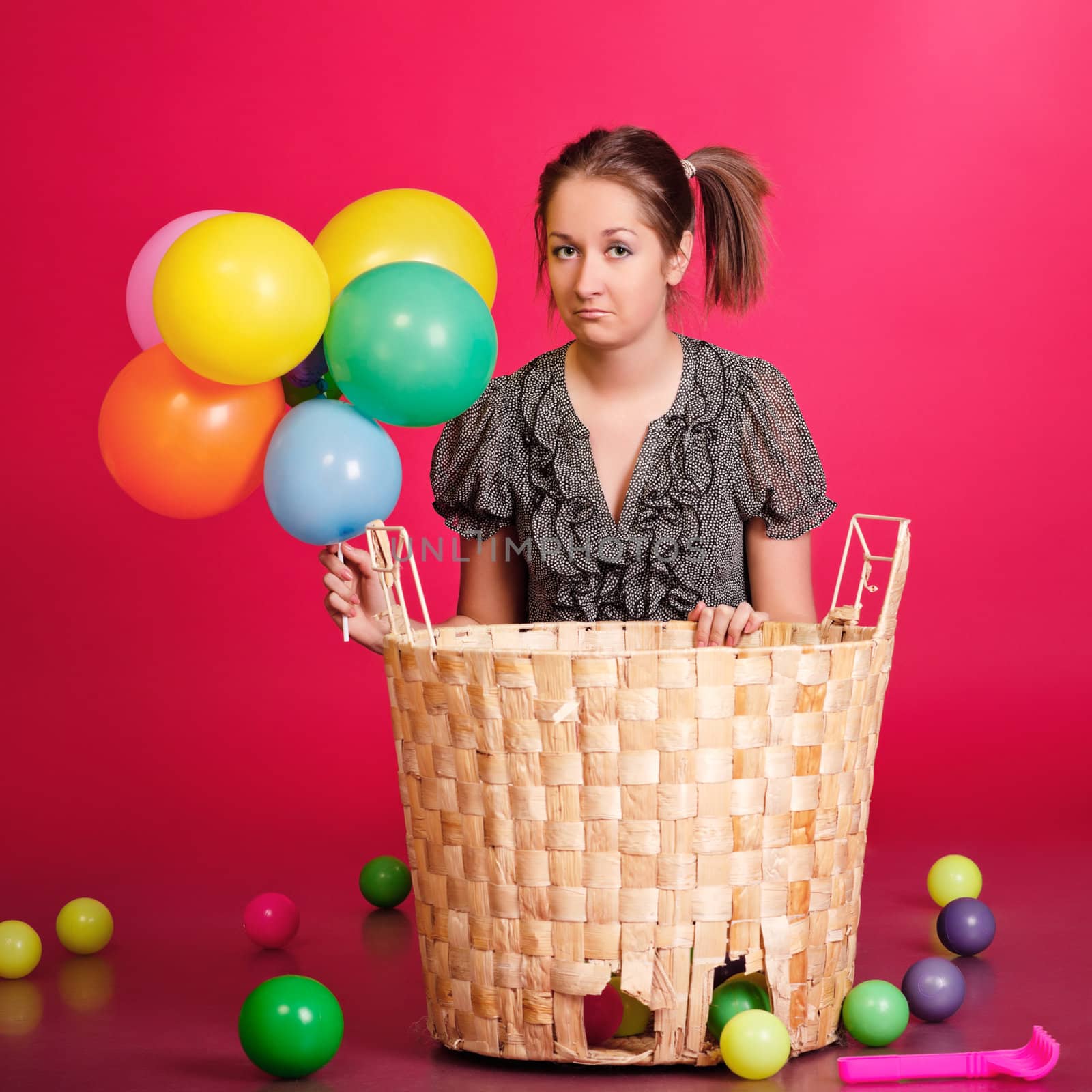 funny girl with basket of toys and balloons, red background