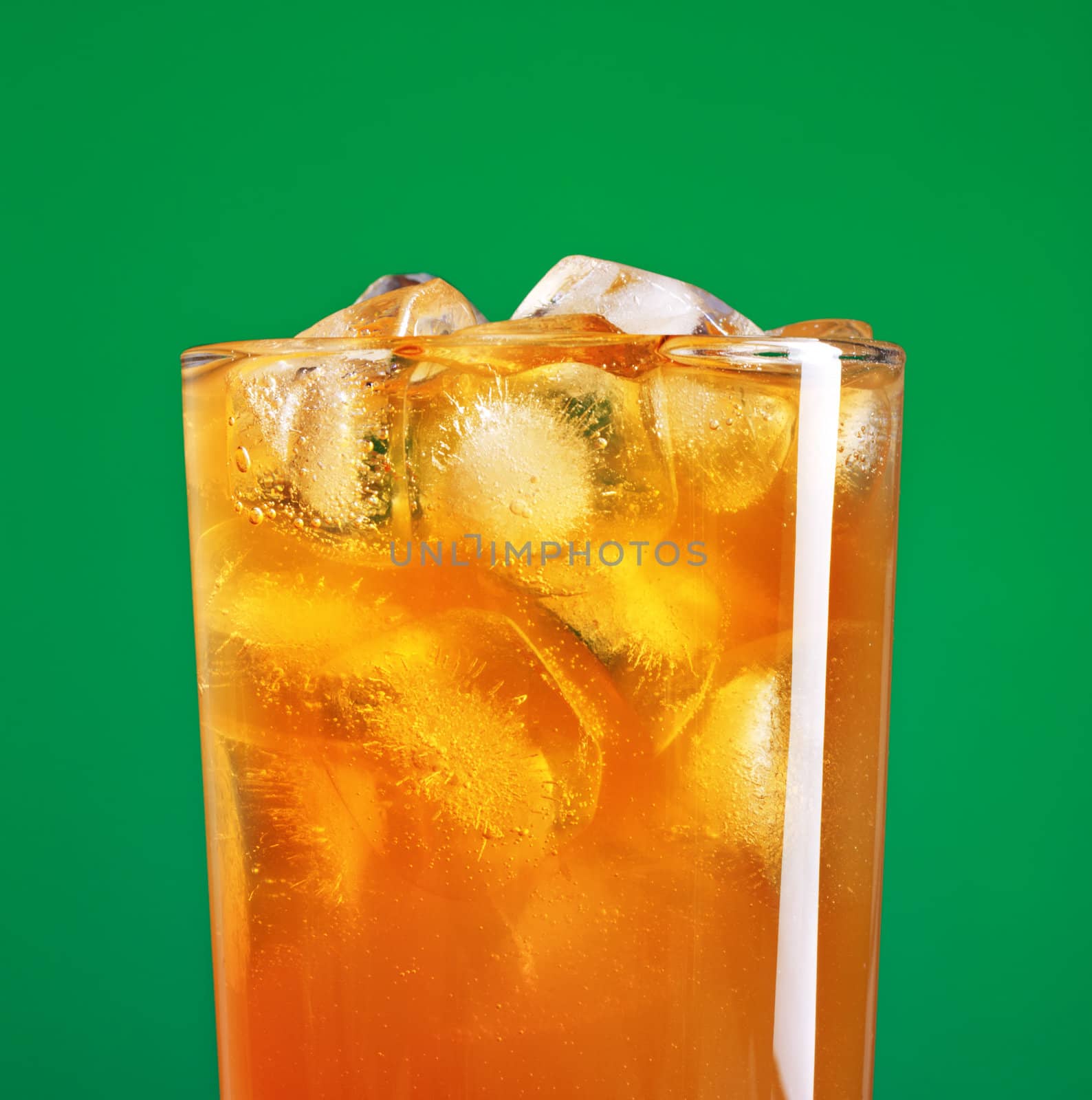 glass of orange soda with ice over green background