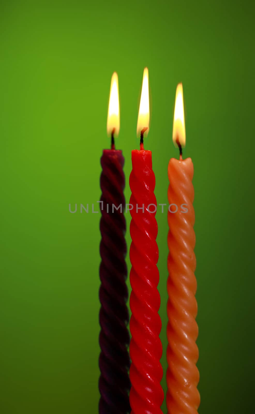 three twisted burning candles over green background