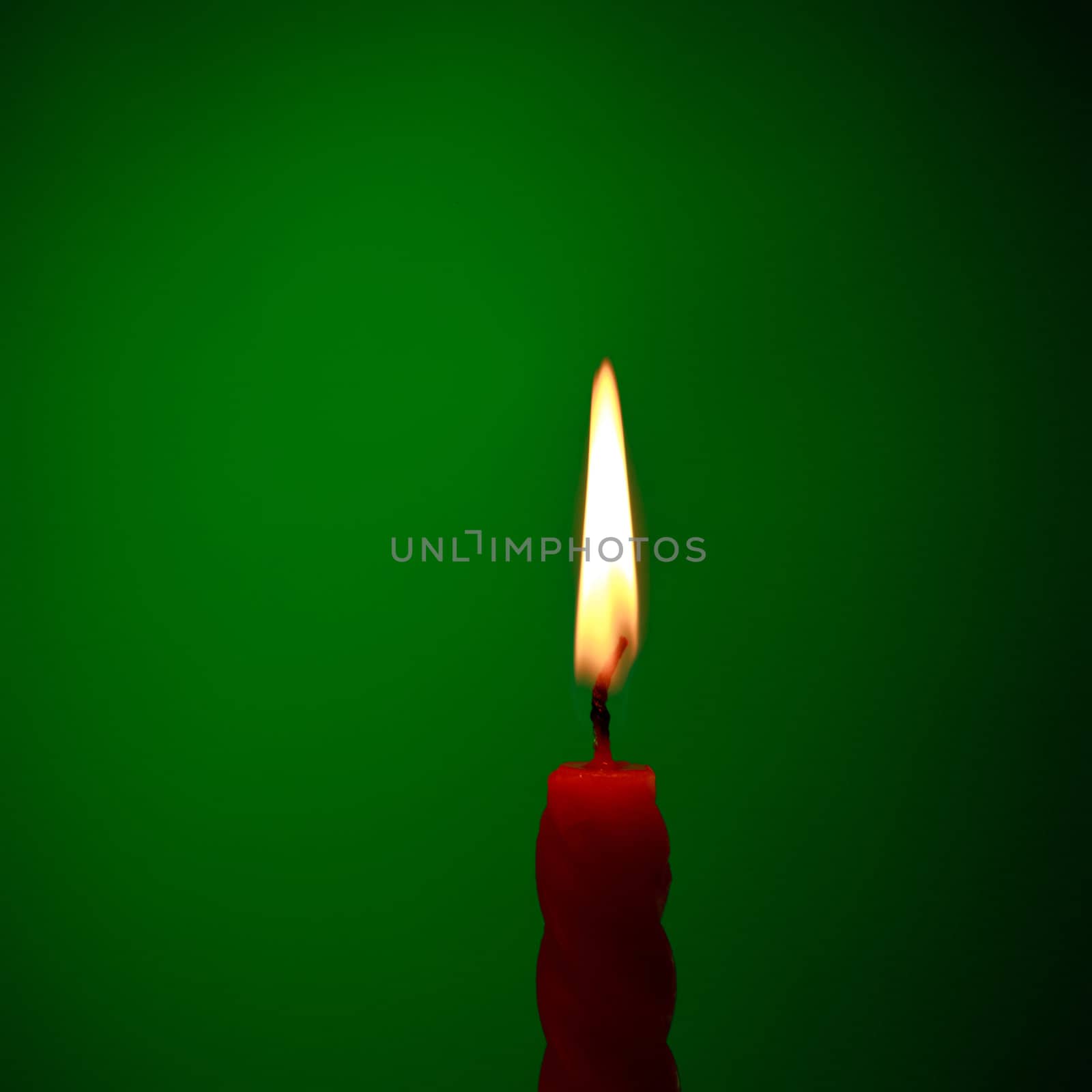 single twisted burning candle over green background