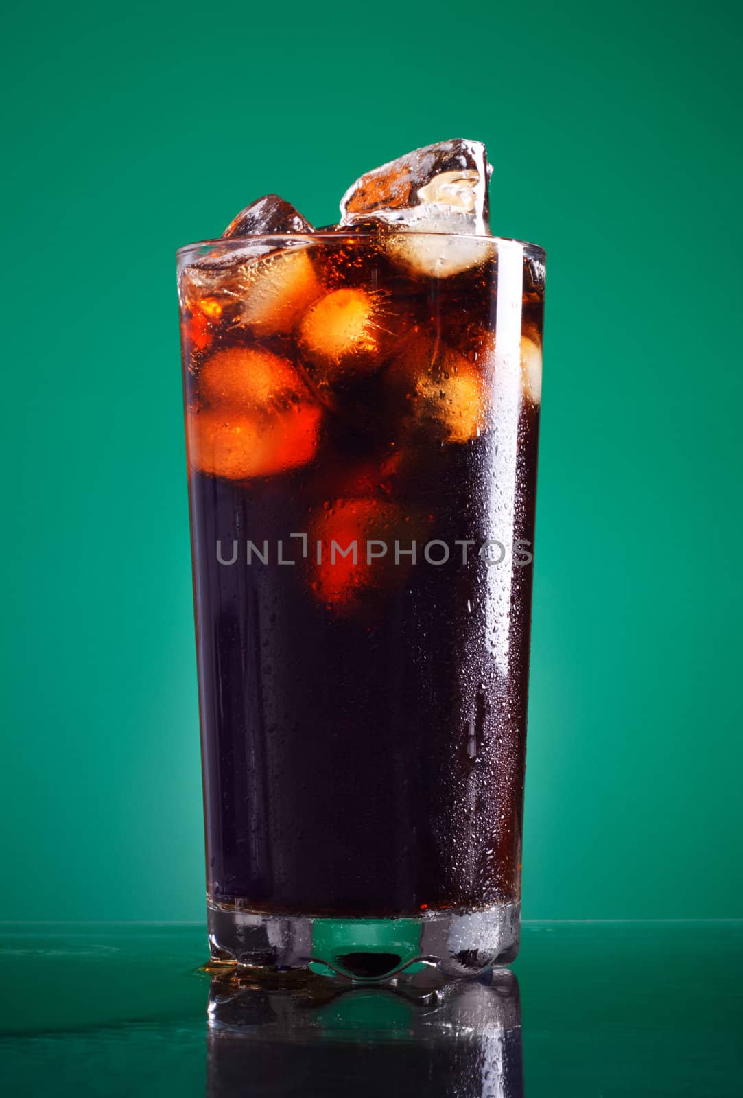 glass of cola with ice on green background