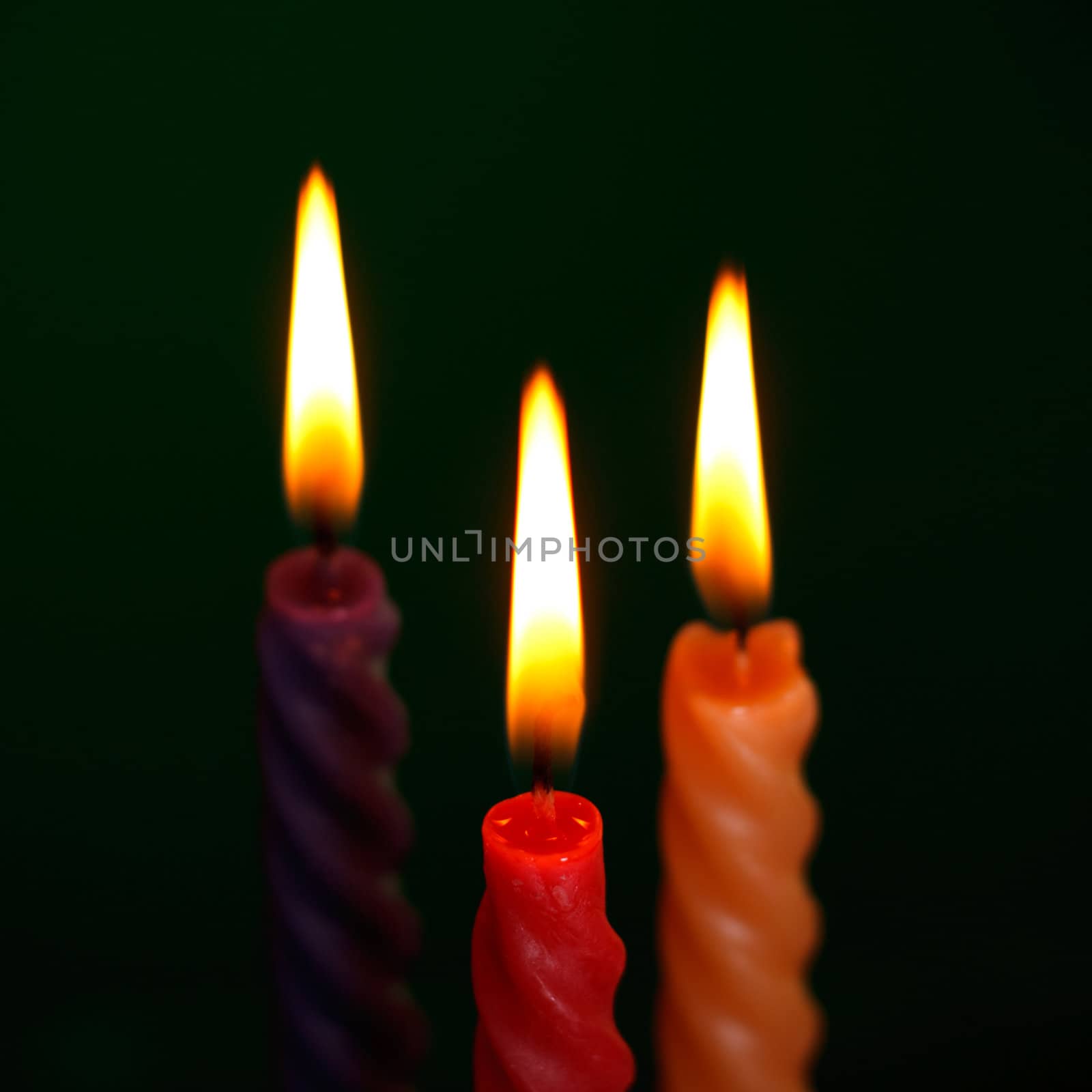 three twisted burning candles over black background