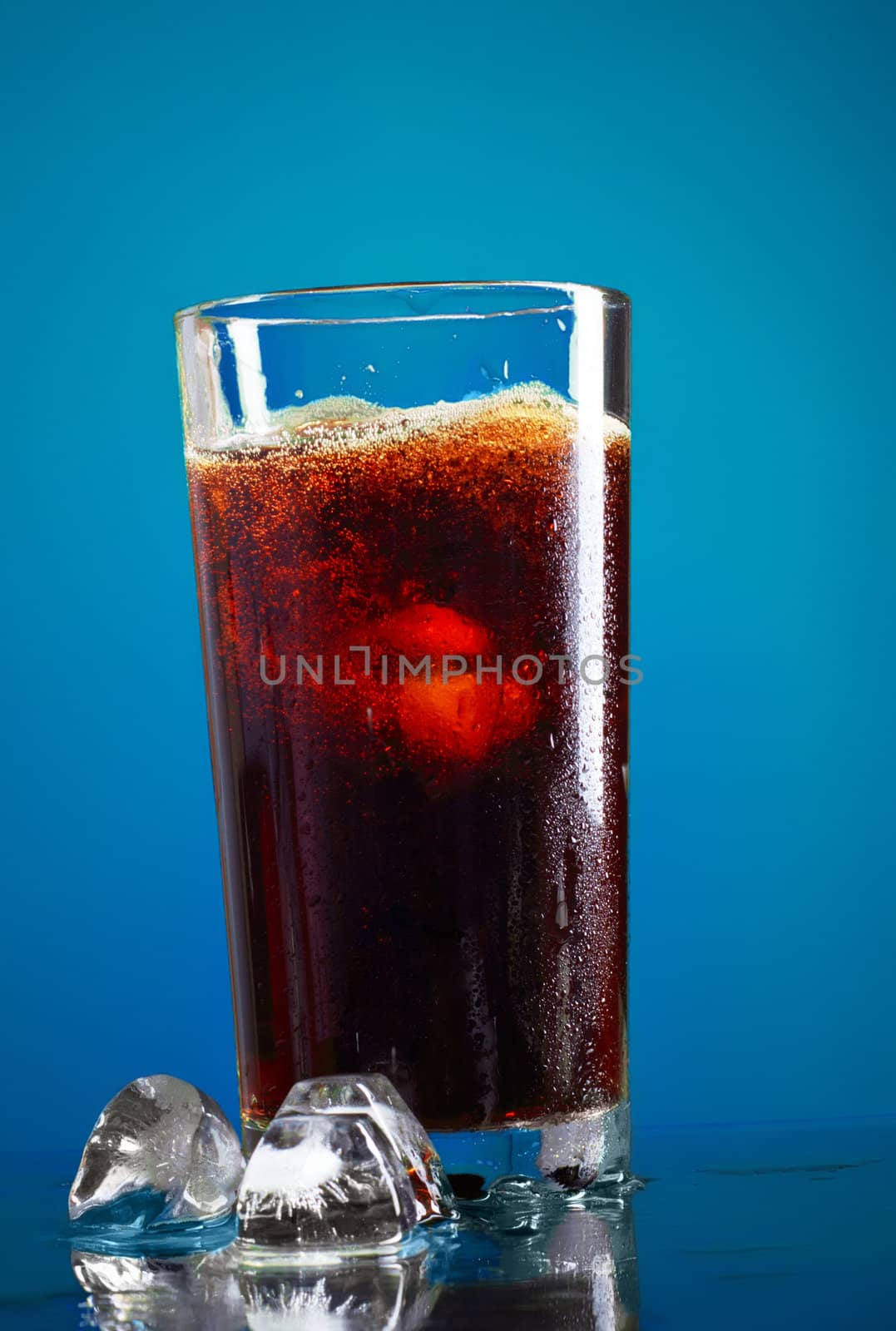 glass of cola with ice on blue background