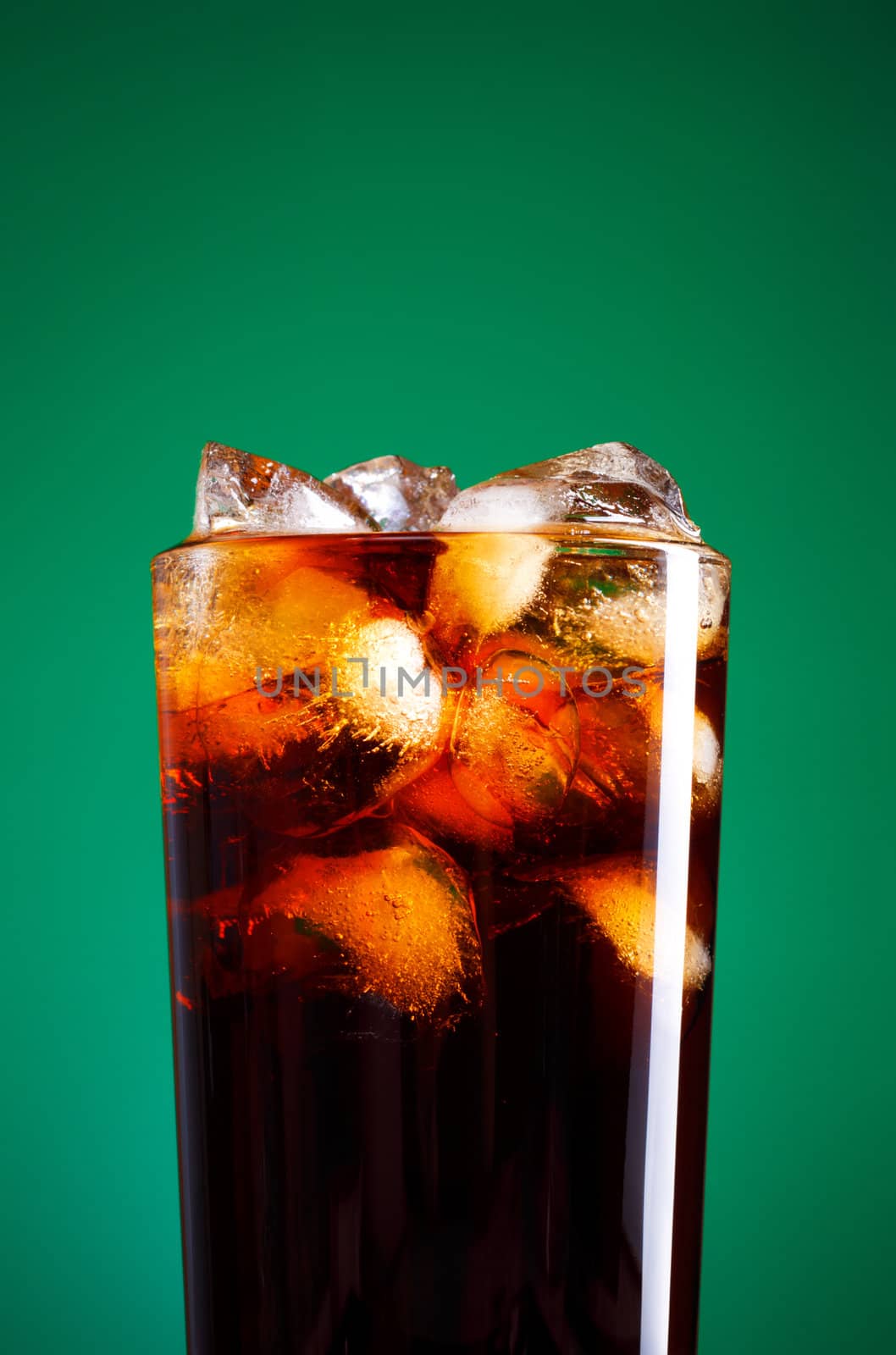 glass of cola with ice on green background