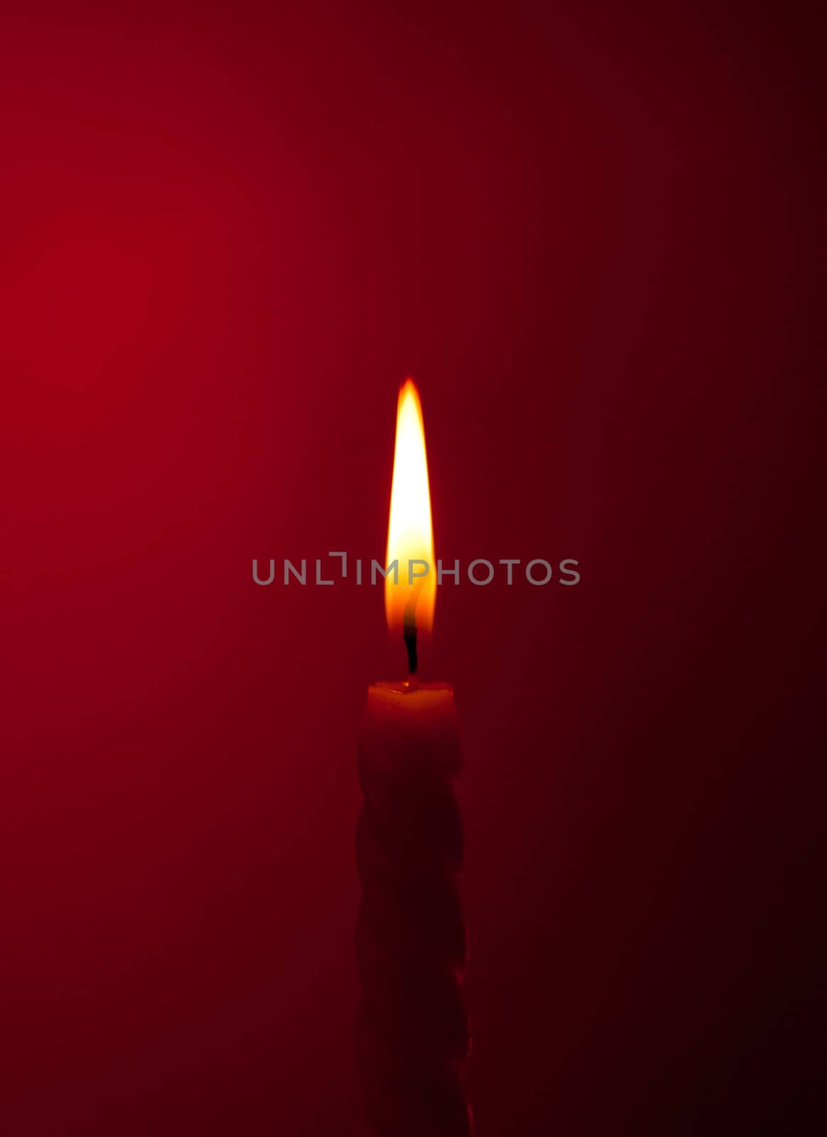 one twisted burning candle over red background