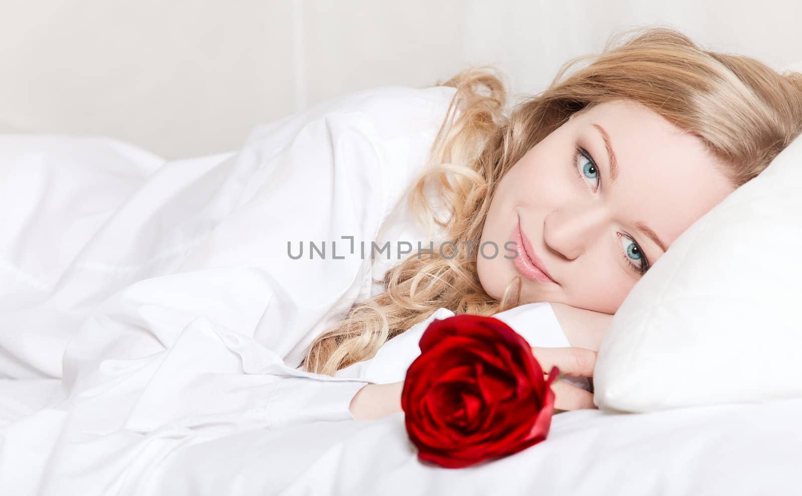 portrait of pretty woman laying in bed with red rose