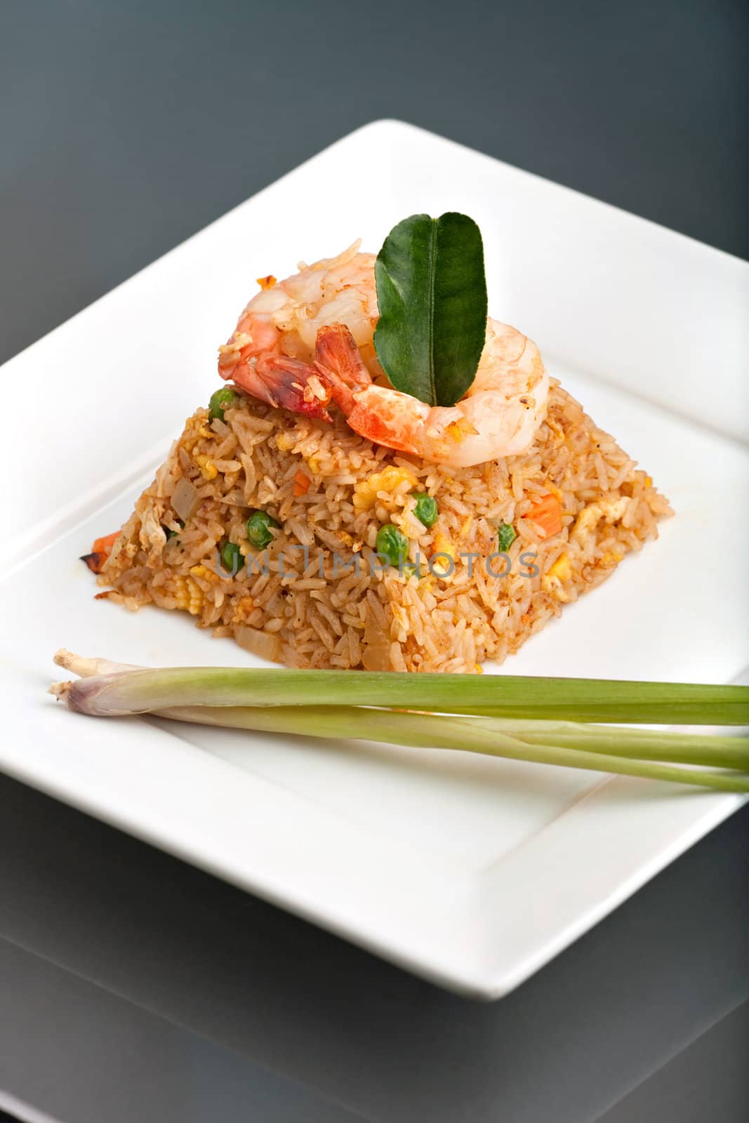 A Thai dish of shrimp fried rice presented on a square white plate in the shape of a pyramid.