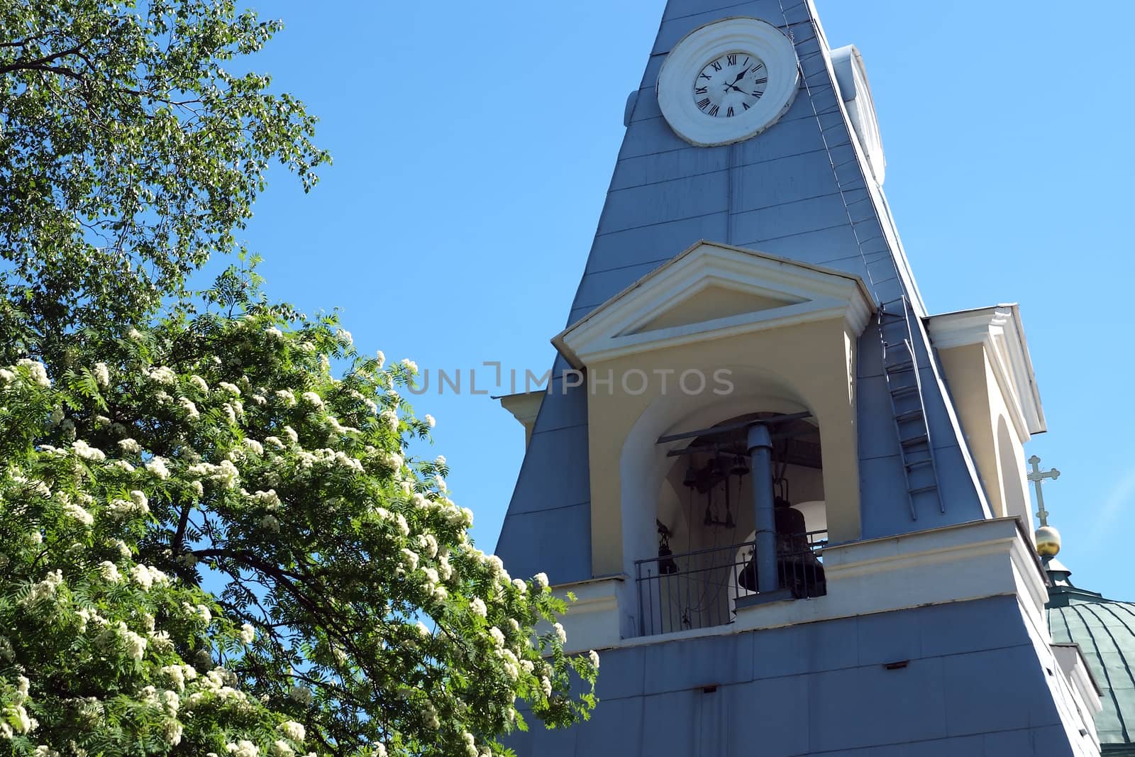 Bell tower with big clock on blue sky background
