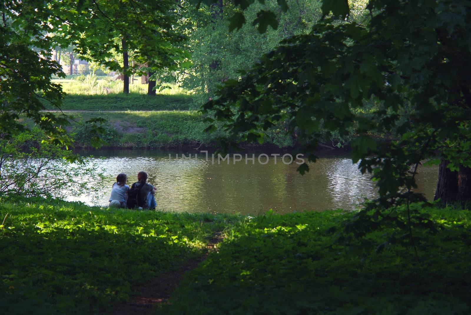 Couple on a lake in park, sitting on a shore and staring on a water