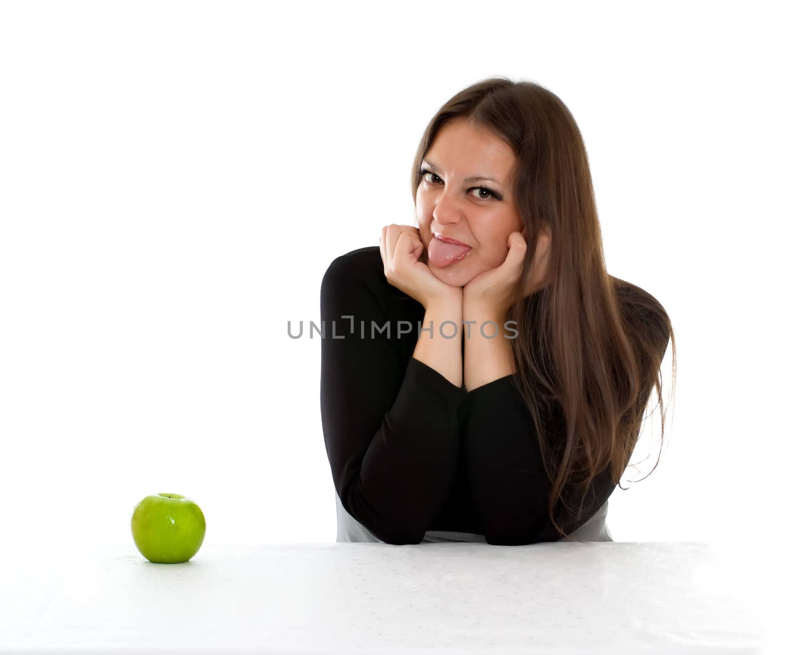 girl sitting at the table with green apple and showing tongue
