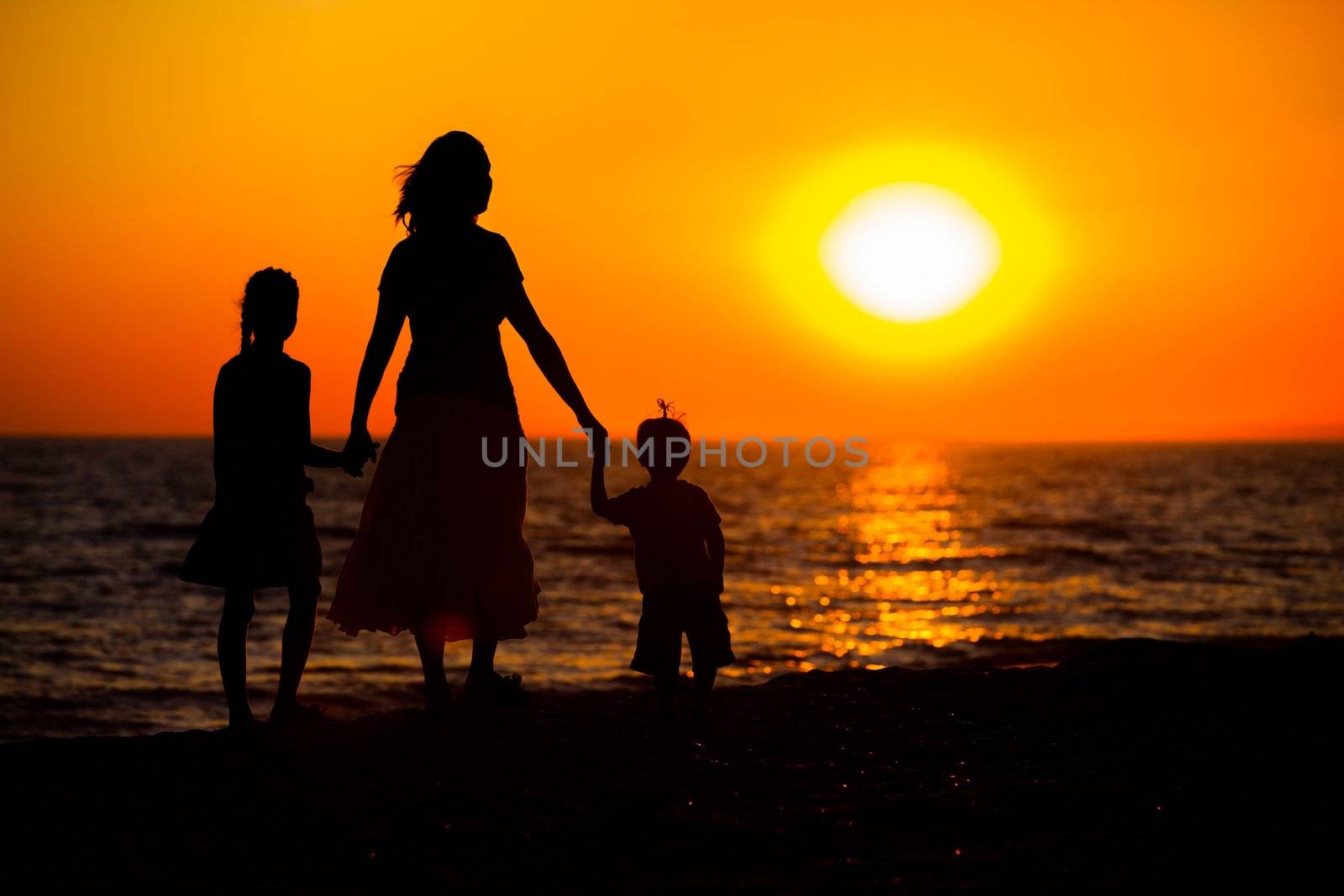 Mother and her kids silhouettes on beach at sunset