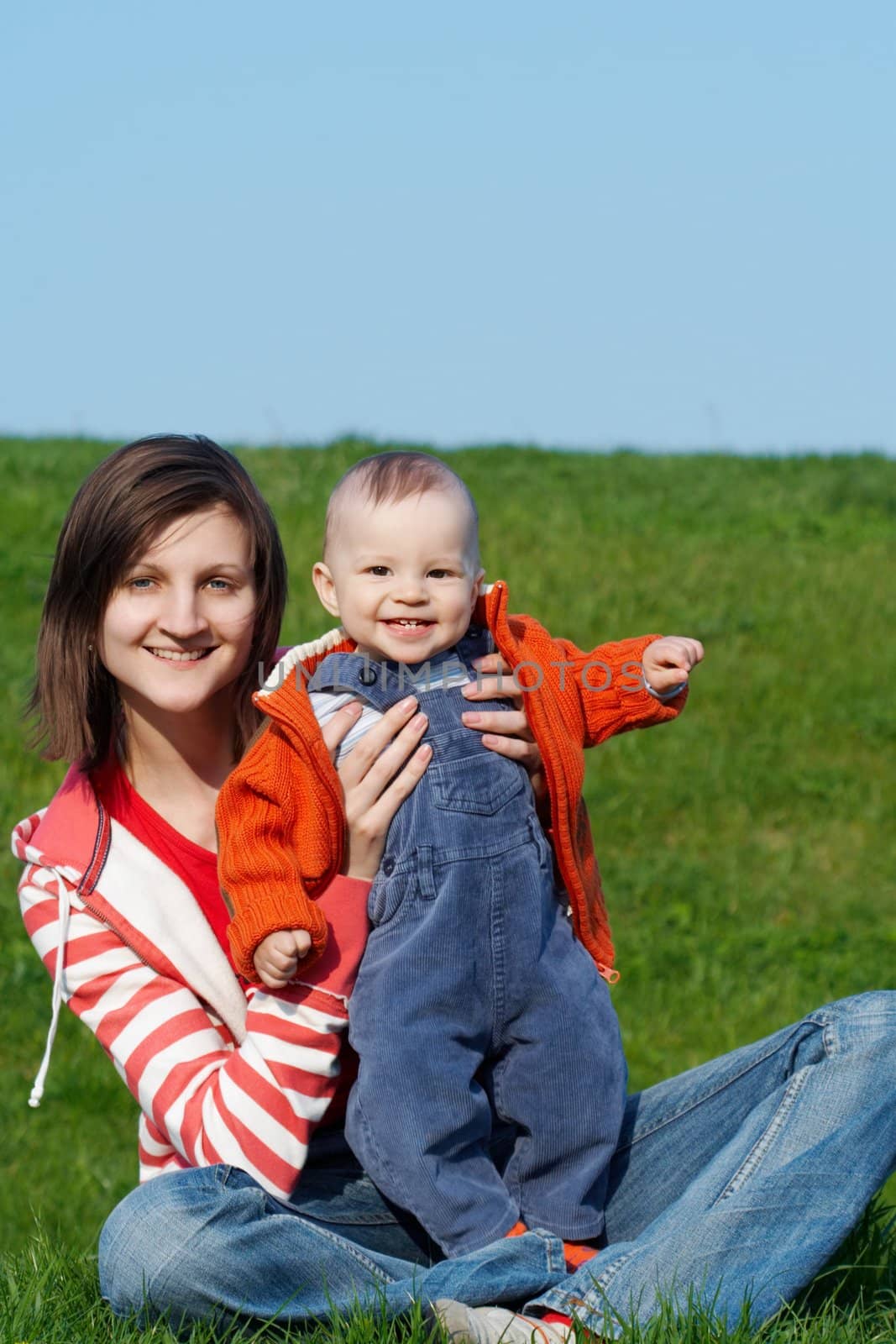 Happy mother with son sitting on green grass by zhu_zhu