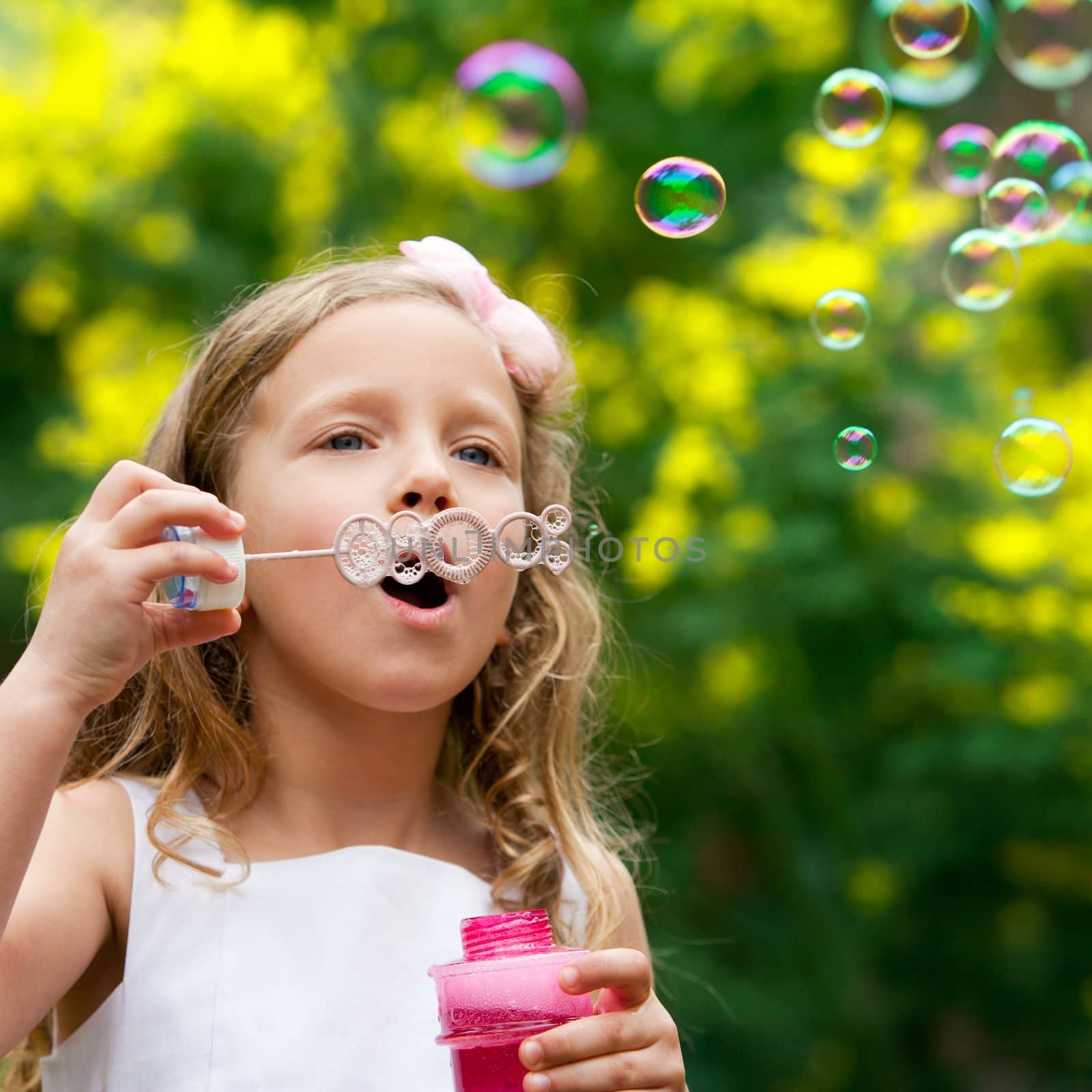 Close up of cute little girl blowing bubbles outdoors.