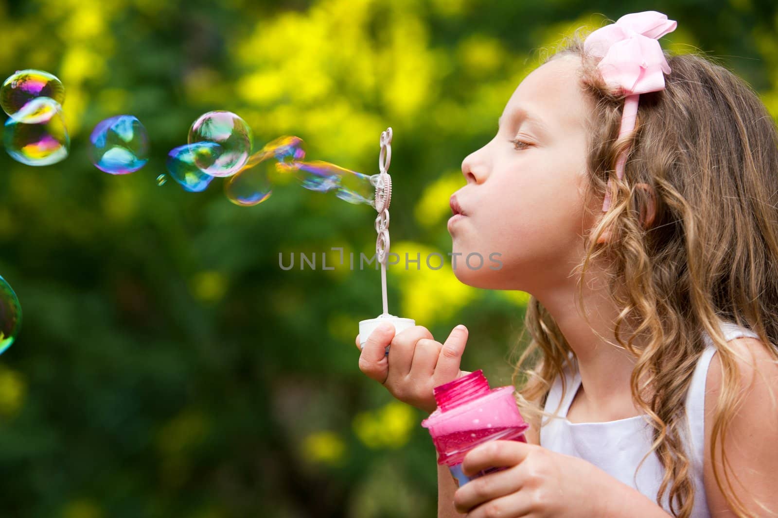 Close up portrait of cute little girl blowing bubbles in garden.
