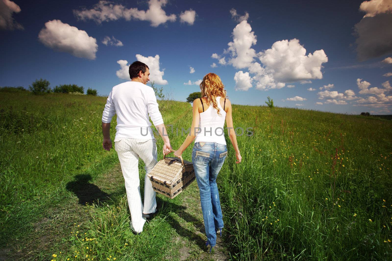 man and woman walk on picnic in green grass