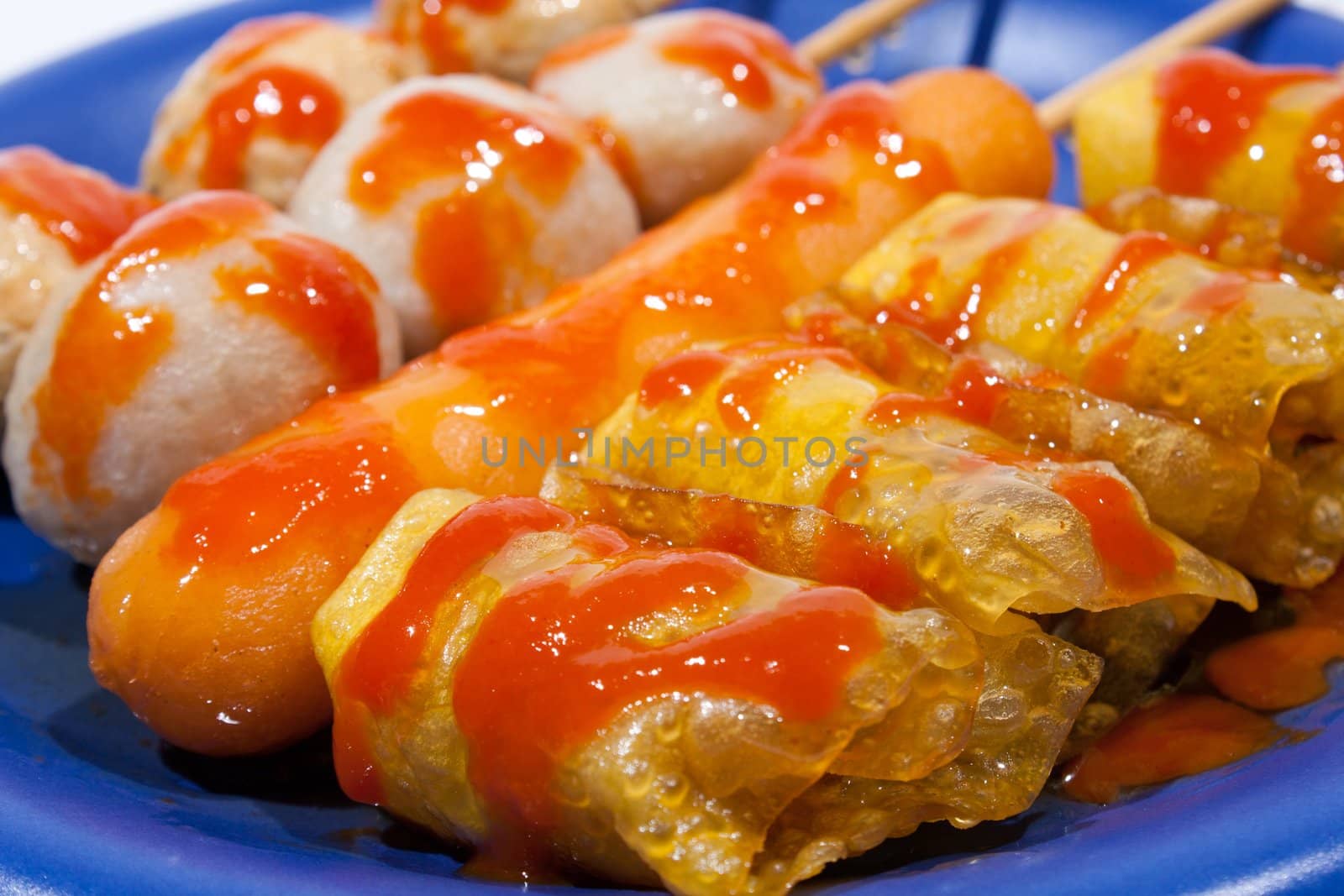 Wet ball grill skewers on the plate topped with spicy sauce placed on a plate. A white background. Blue needle plate.