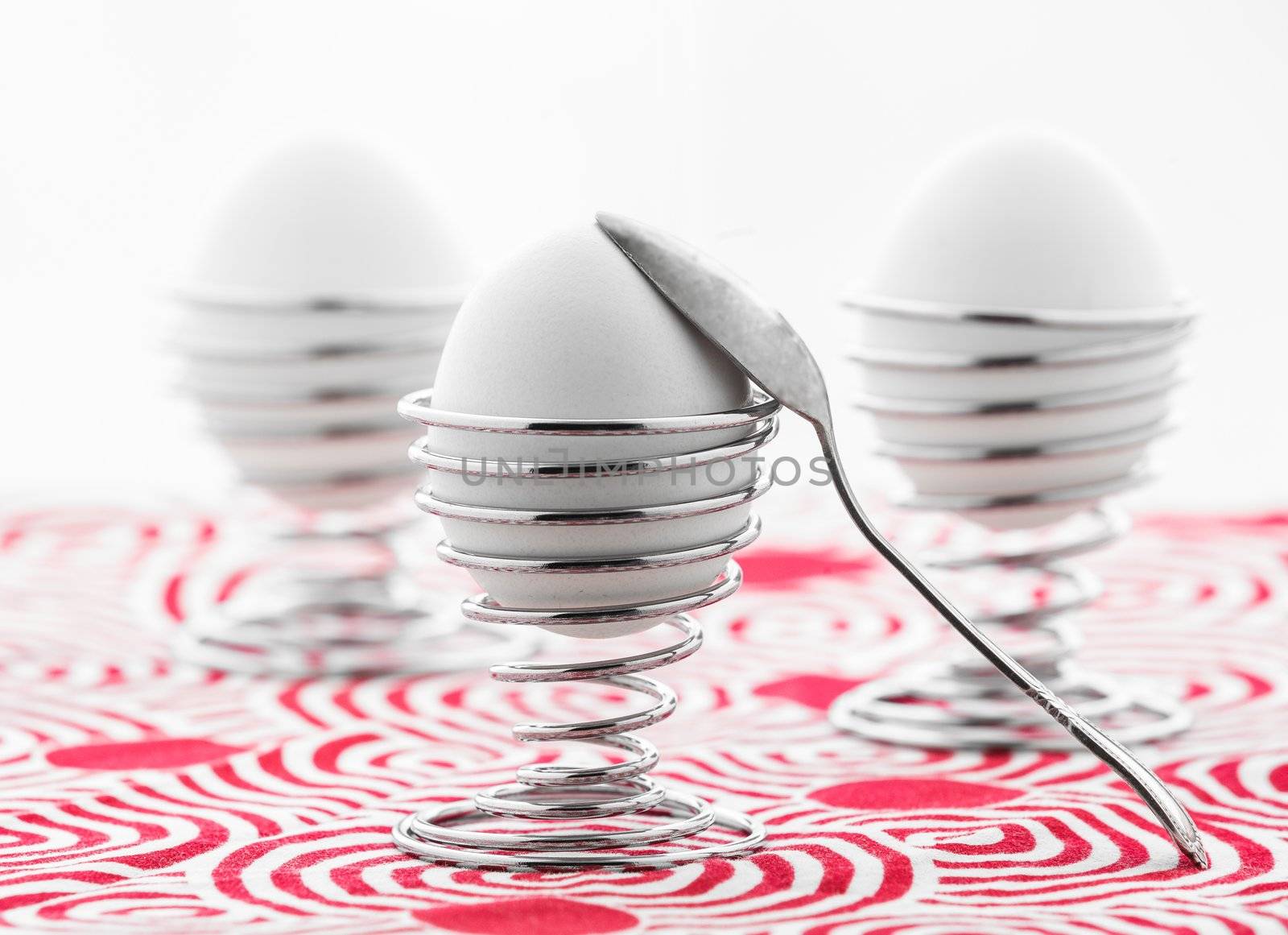 Three eggs in metal stands with a spoon