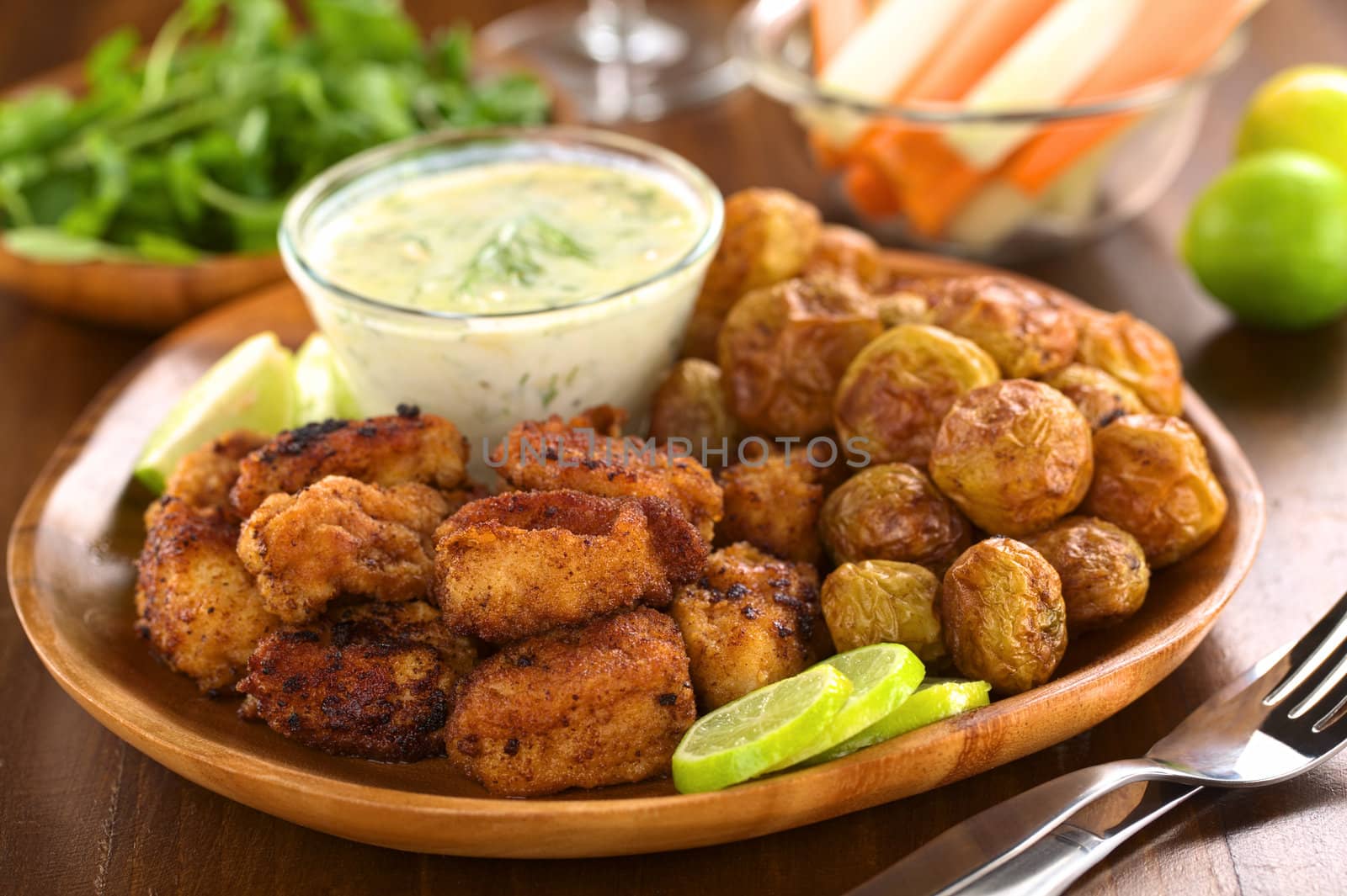 Breaded fried calamary pieces with small baked potatoes and tzatziki (Selective Focus, Focus on the front of the upper calamary and the first potato on the right)