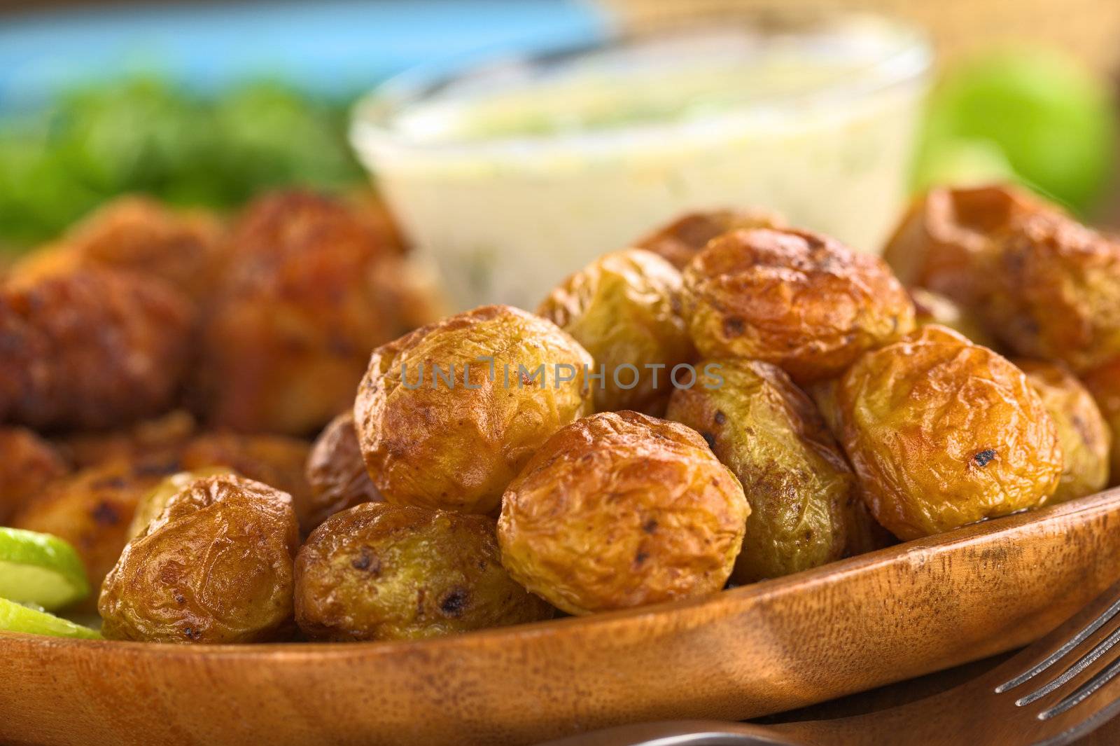 Small baked potatoes with fried breaded calamary and tzatziki in the back (Selective Focus, Focus on the potato in the middle and the one on the left of the image)