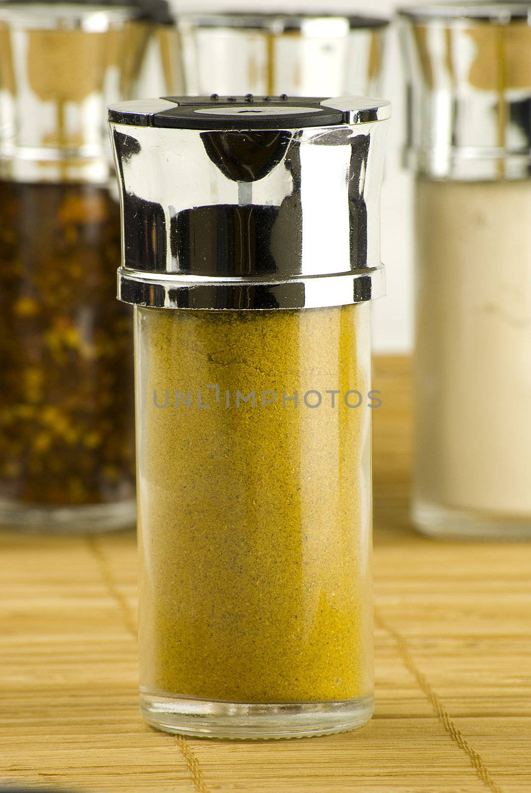curry powder in a glass jar on different spices background over wooden mat