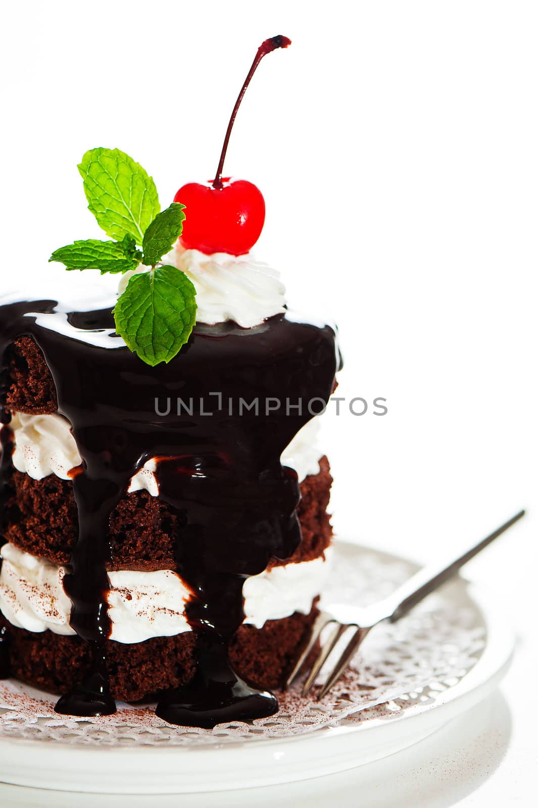 A small chocolate cake with 2 layer white cream, cherry and mint  on top on a white background as a studio shot
